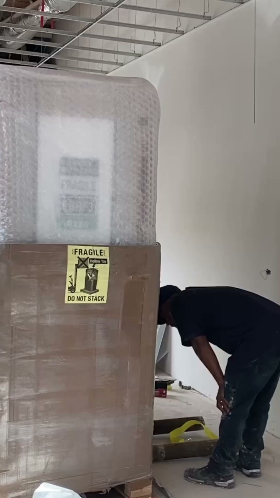Worker bending over near a wrapped pallet in a warehouse aisle