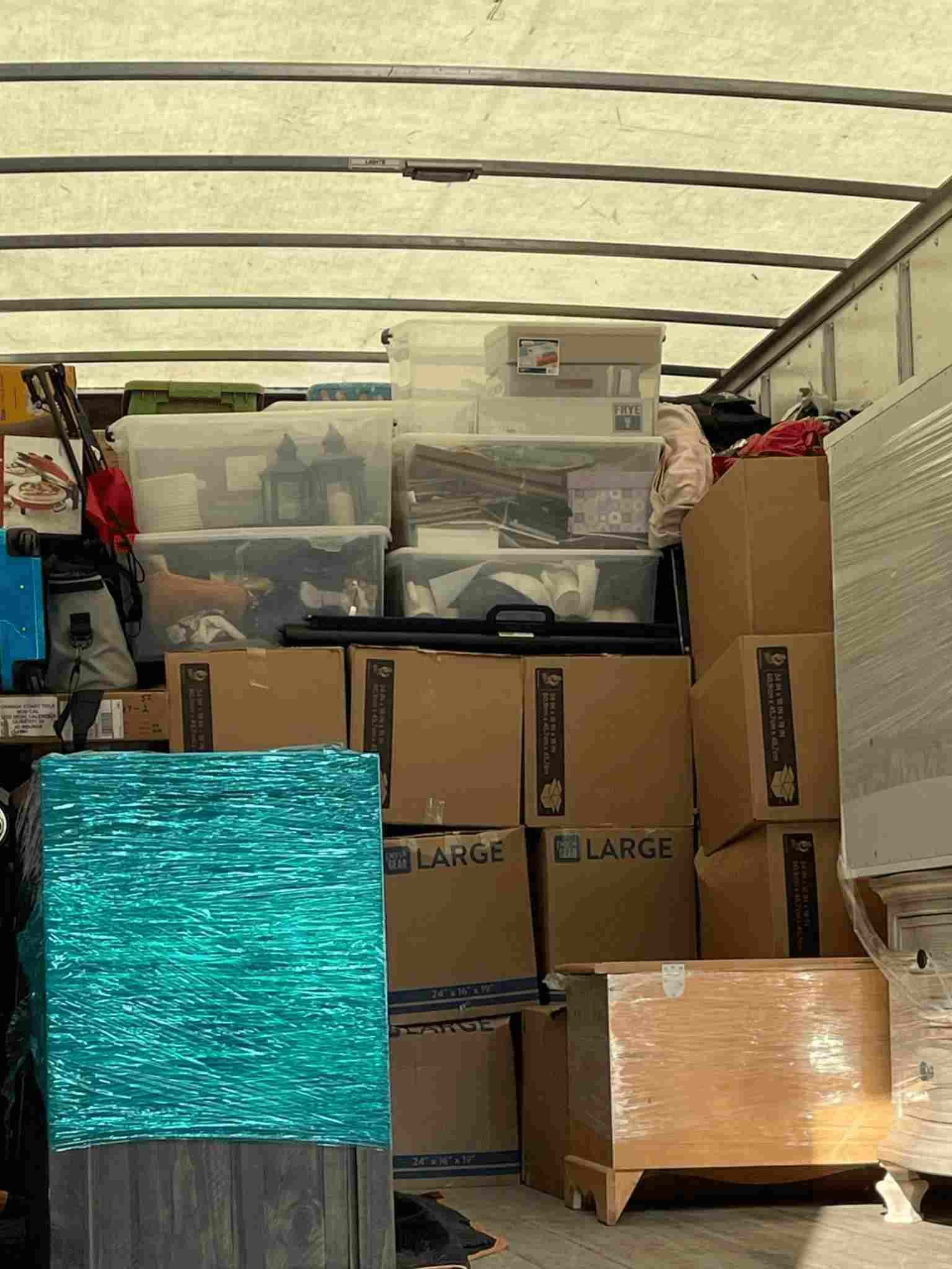 Packed moving truck with stacked boxes, plastic storage bins, and a turquoise bag under a striped canopy.
