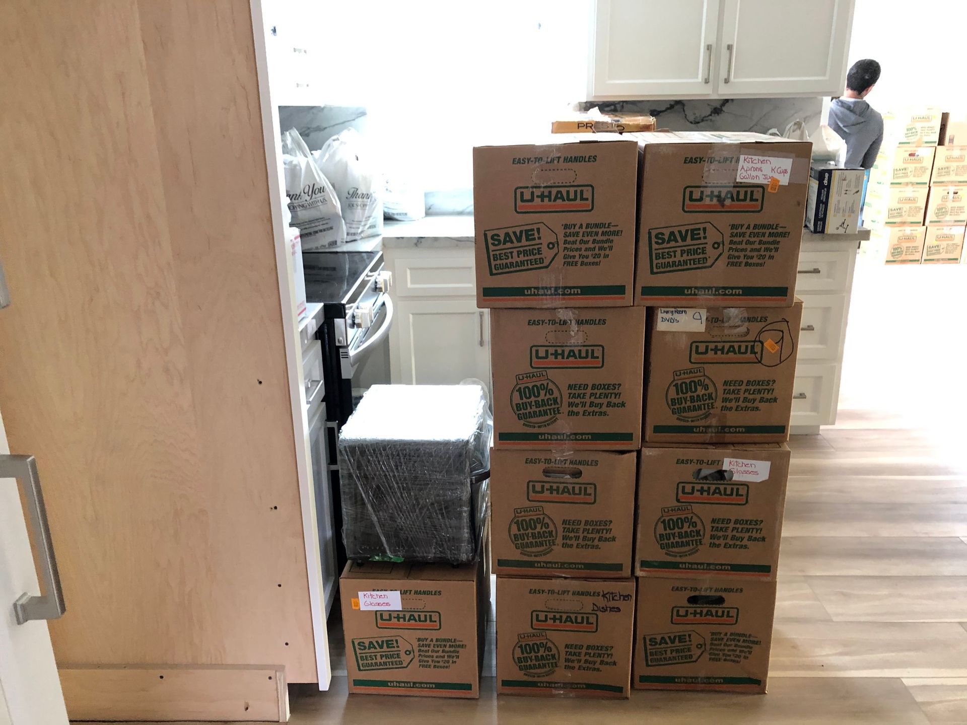 Stacked moving boxes in a kitchen, with a person in the background.