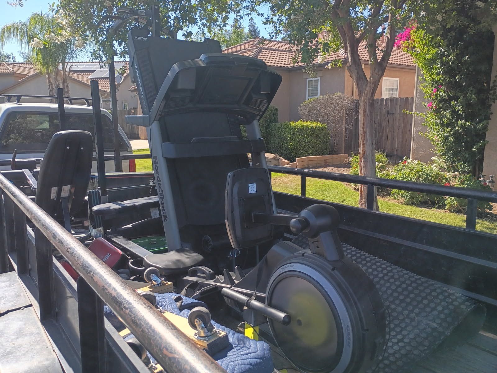 Black off-road vehicle chassis in a trailer, with a large tire and engine parts outdoors.
