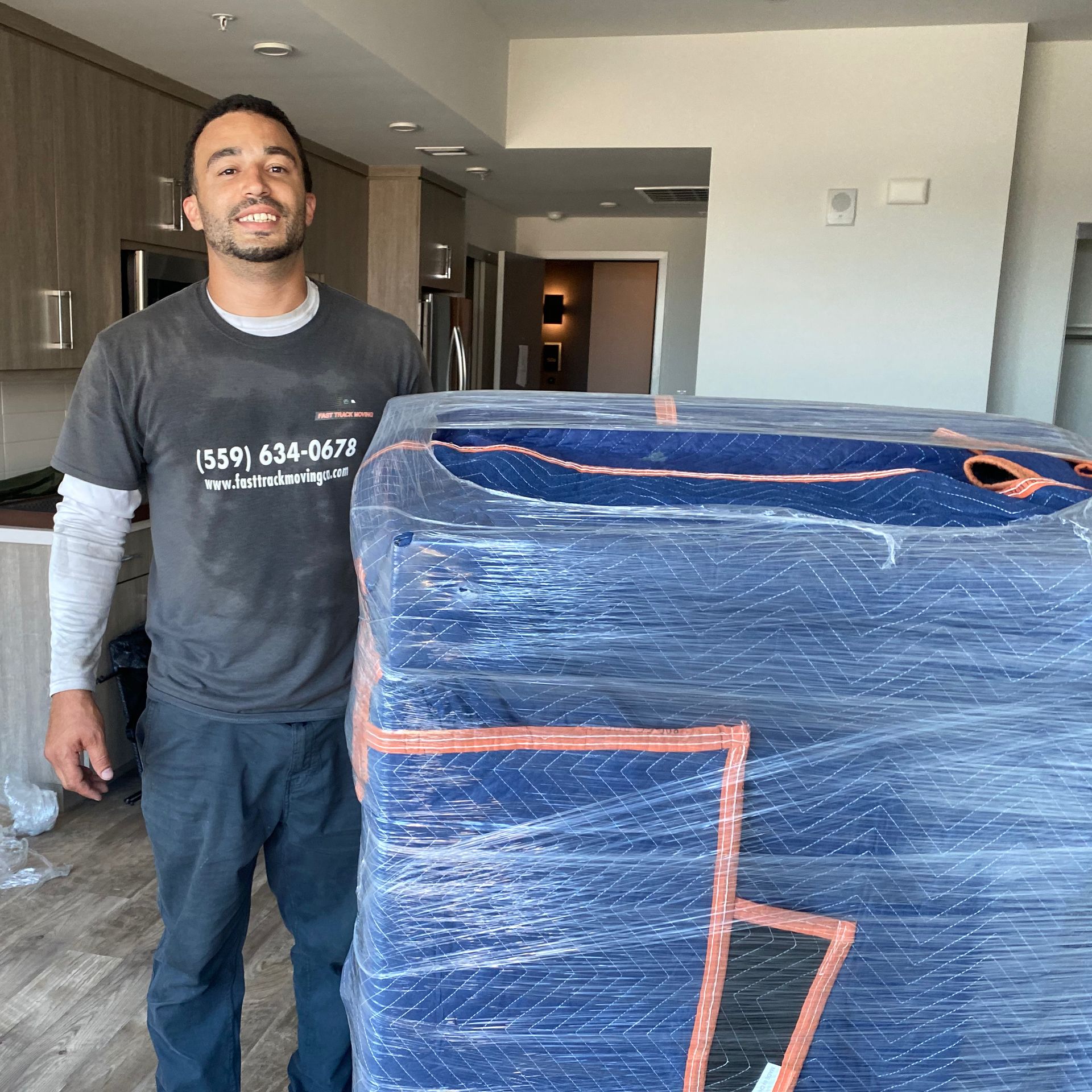 Man standing beside a plastic-wrapped blue couch in a modern apartment