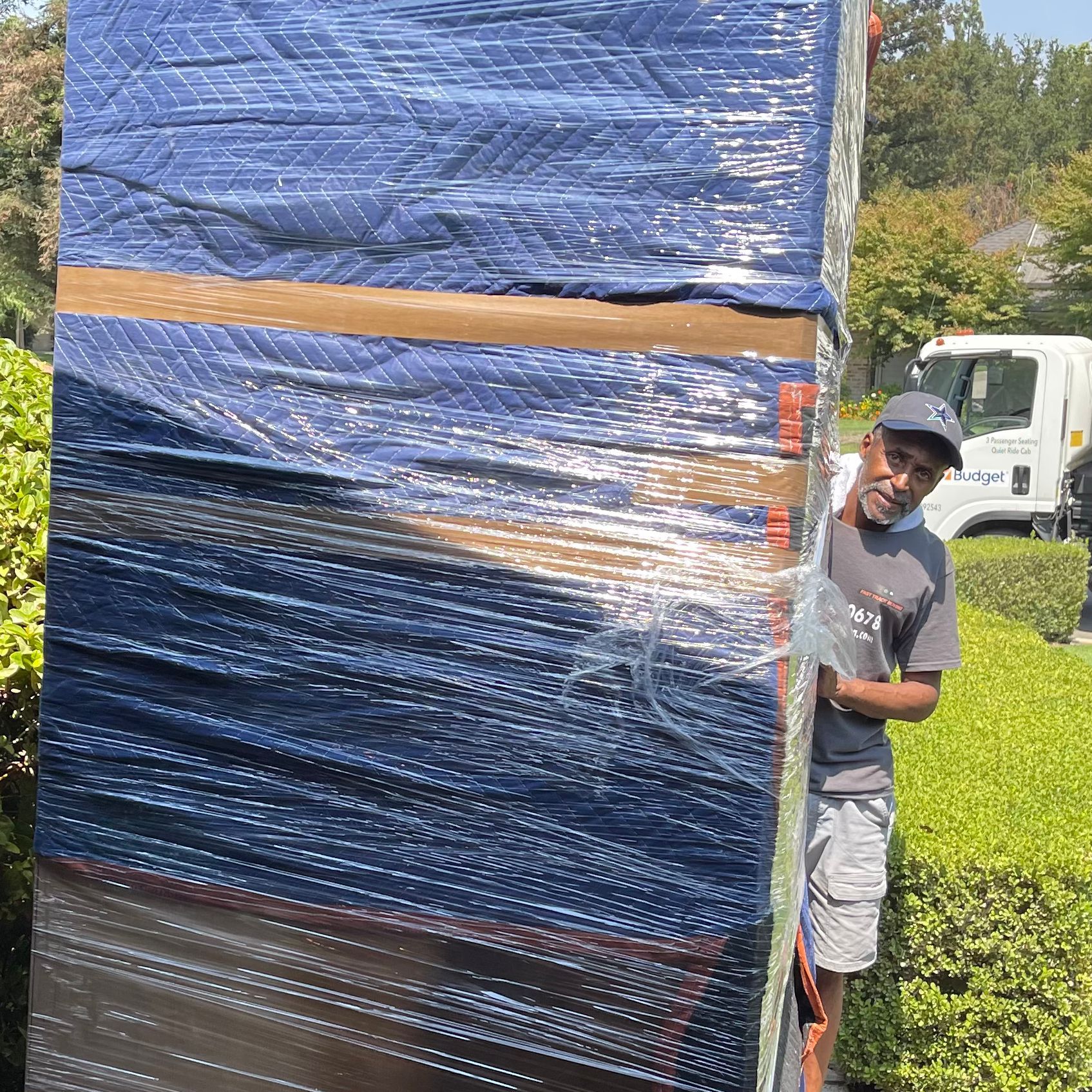 Worker peeks from behind a large blue-wrapped crate outdoors