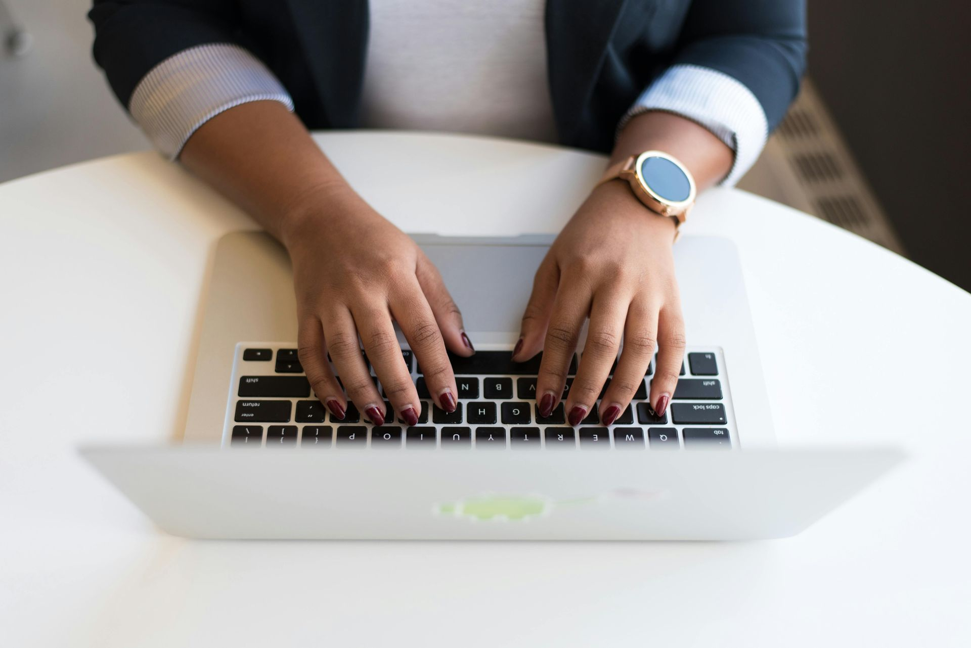 Pessoa digitando em um laptop com esmalte escuro e usando um relógio.
