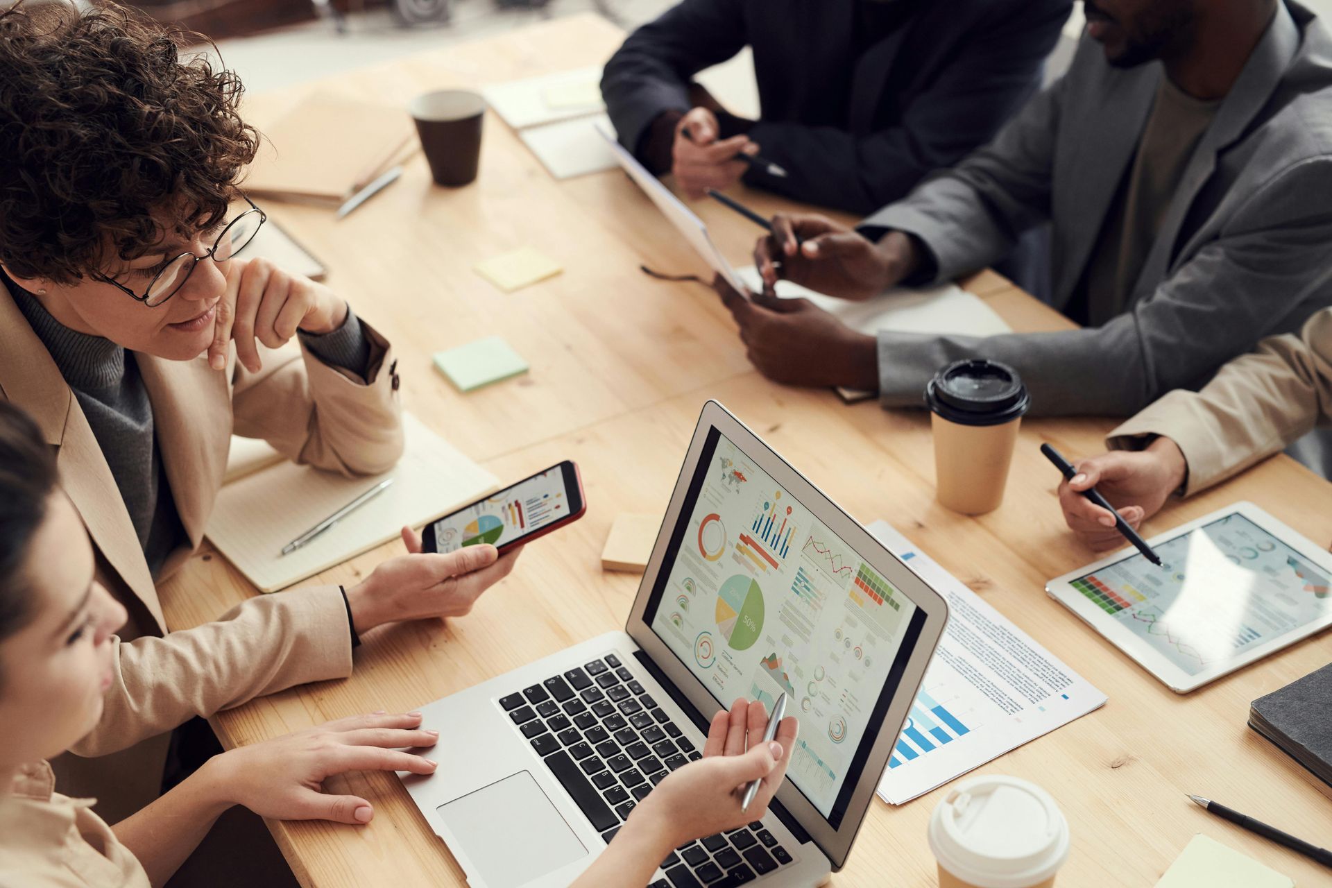 Equipe de negócios analisa dados em laptop e celular em uma mesa, discutindo gráficos.