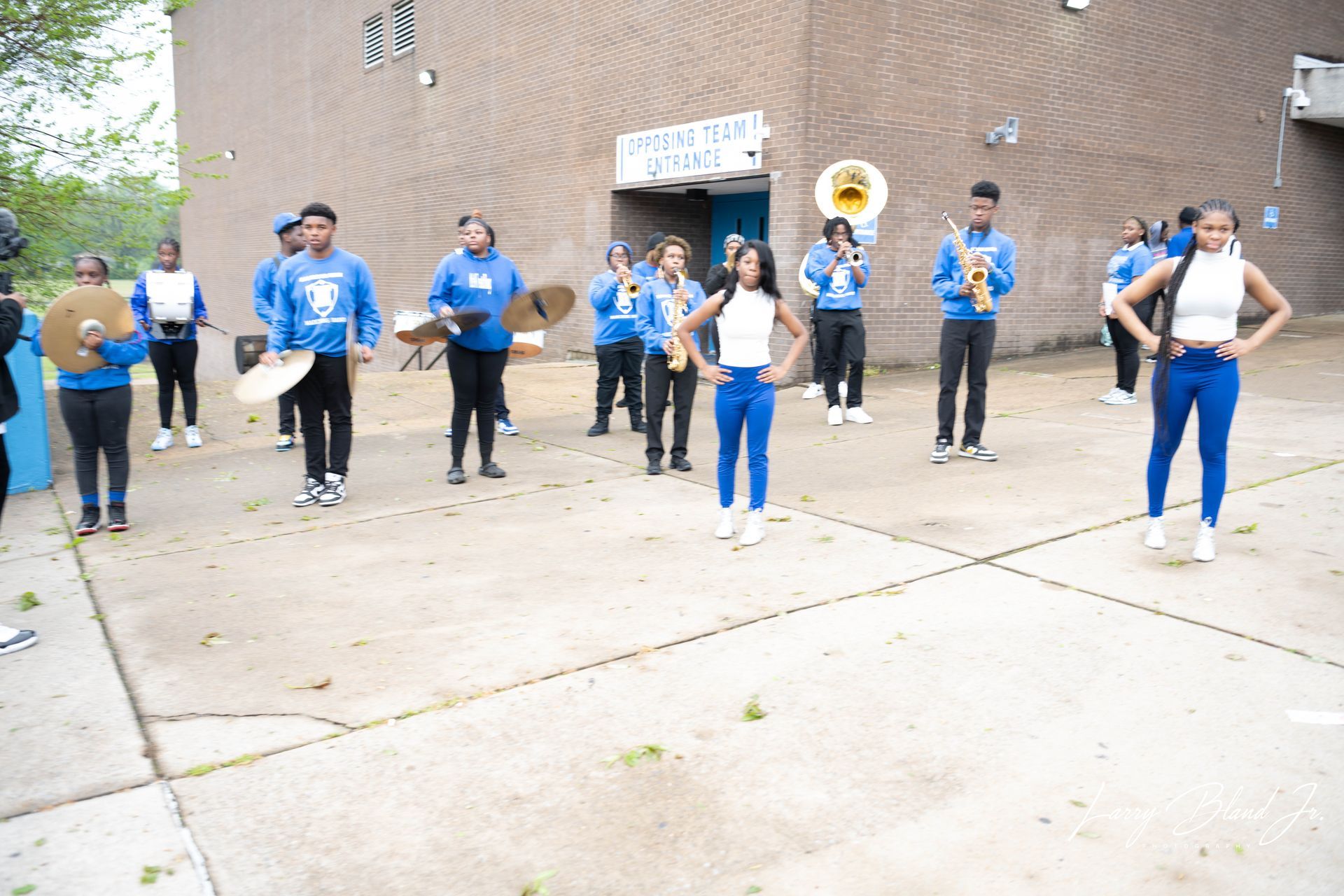 School band in blue uniforms performing outdoors, instruments visible.