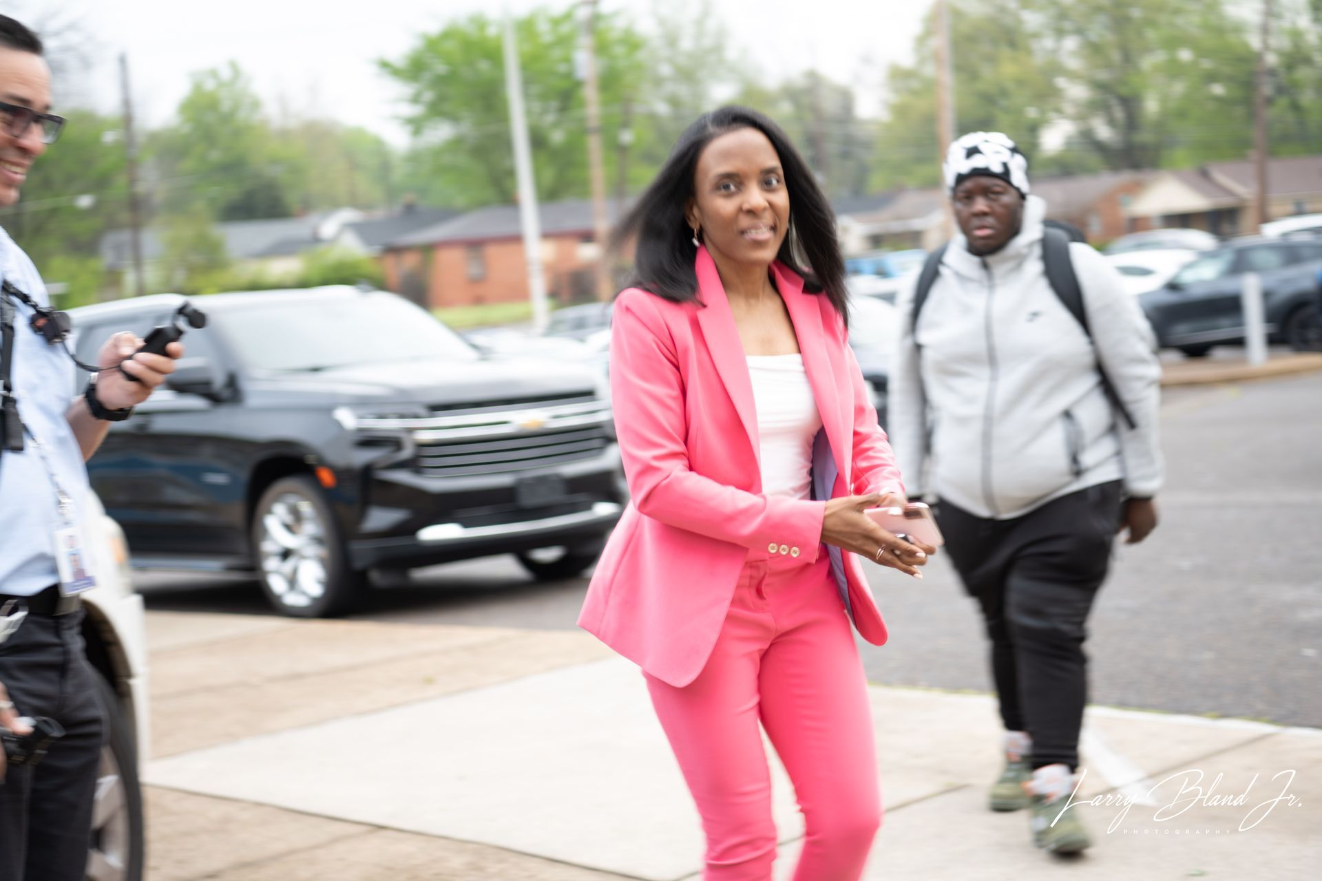Woman in pink suit smiles, walking towards the camera. .