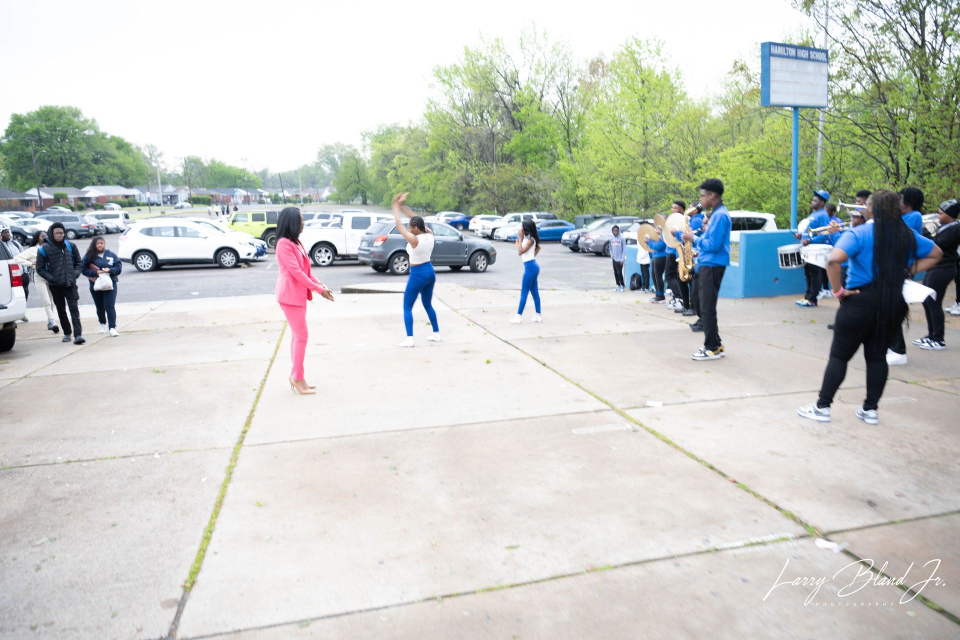 People in blue and pink outfits outdoors, posing in front of a school building.