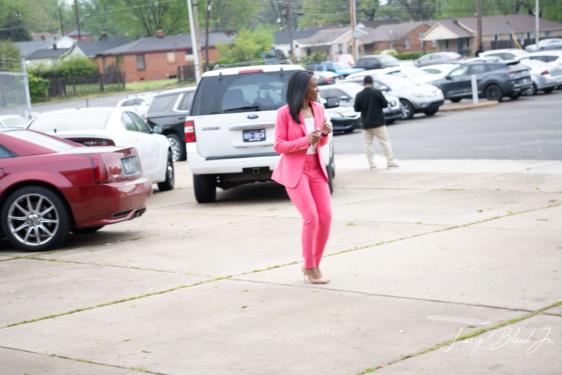 Woman in pink suit walking in parking lot; cars in background.