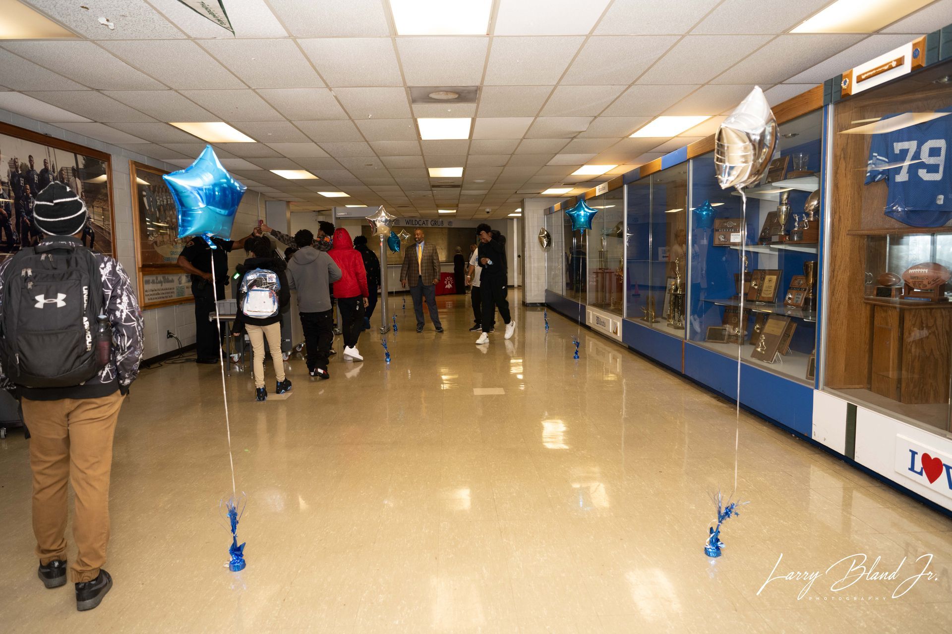 People walking down a hallway with display cases. Blue balloons attached to the floor.