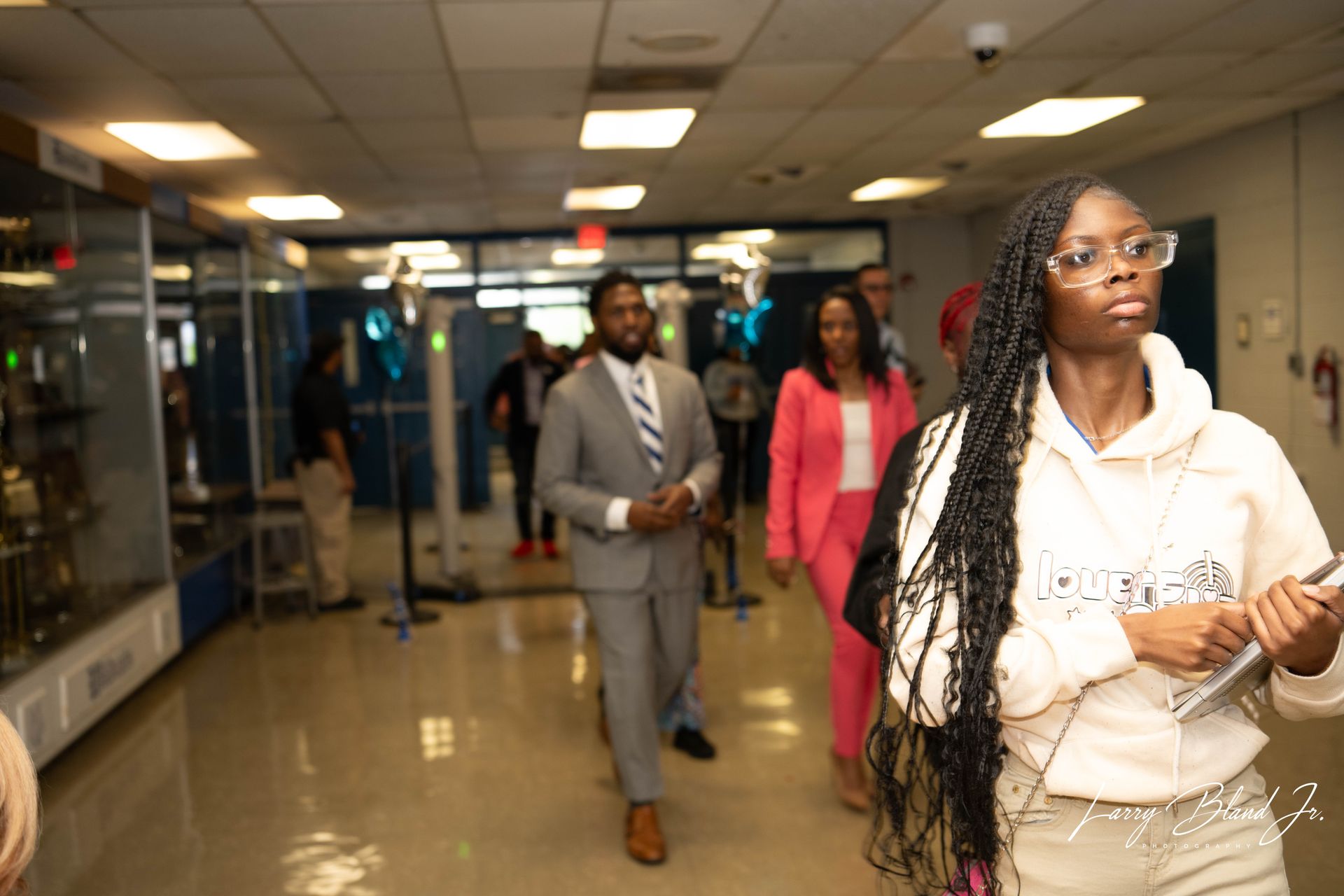 People walking down a school hallway; a man in a suit leads, others follow.