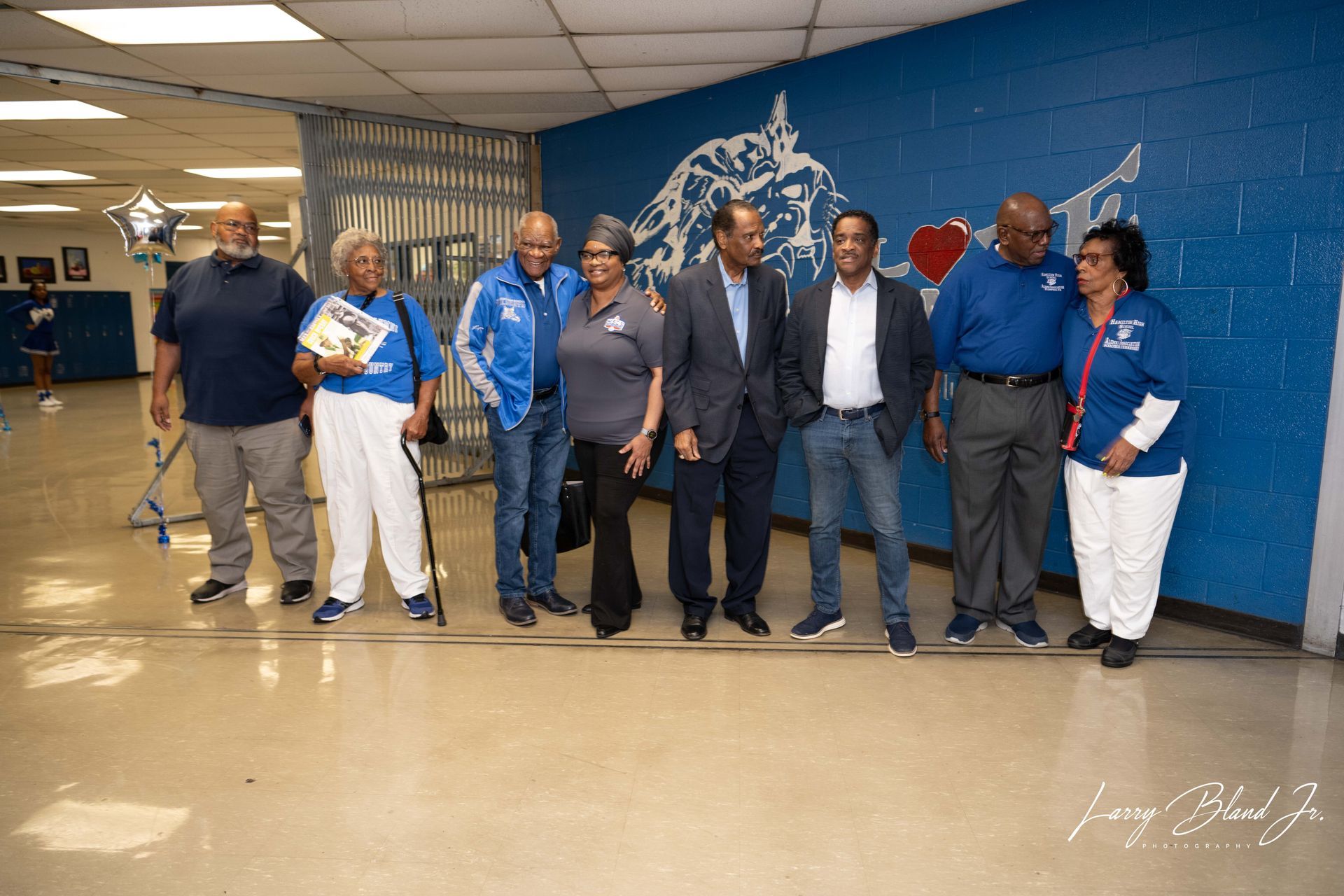 Group of people posing for a photo in a school hallway, with a blue mural on the wall.