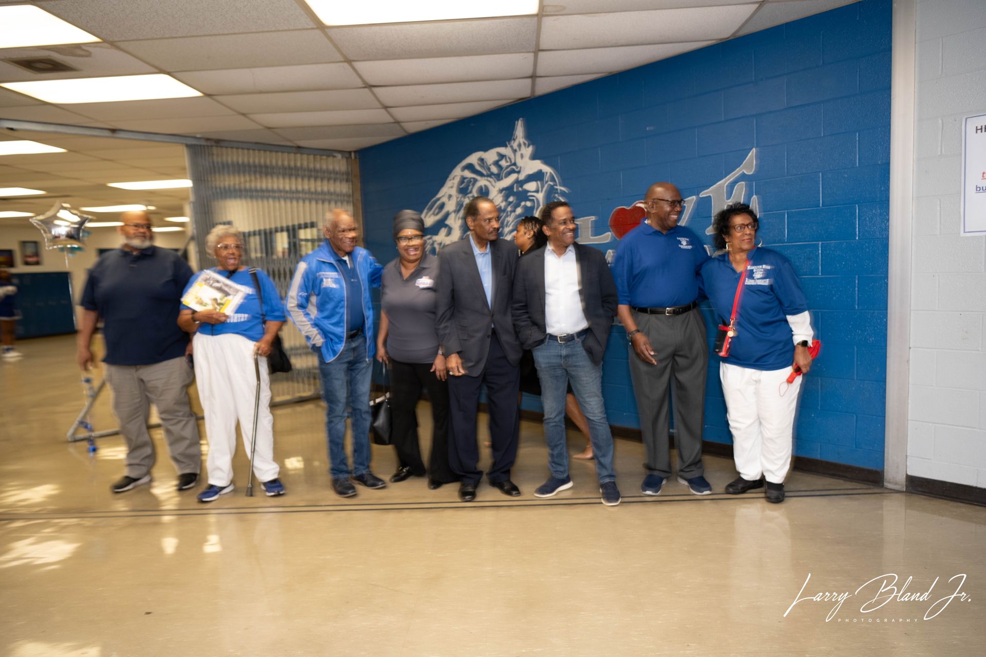 Group of people standing in a hallway in front of a blue wall with a logo.