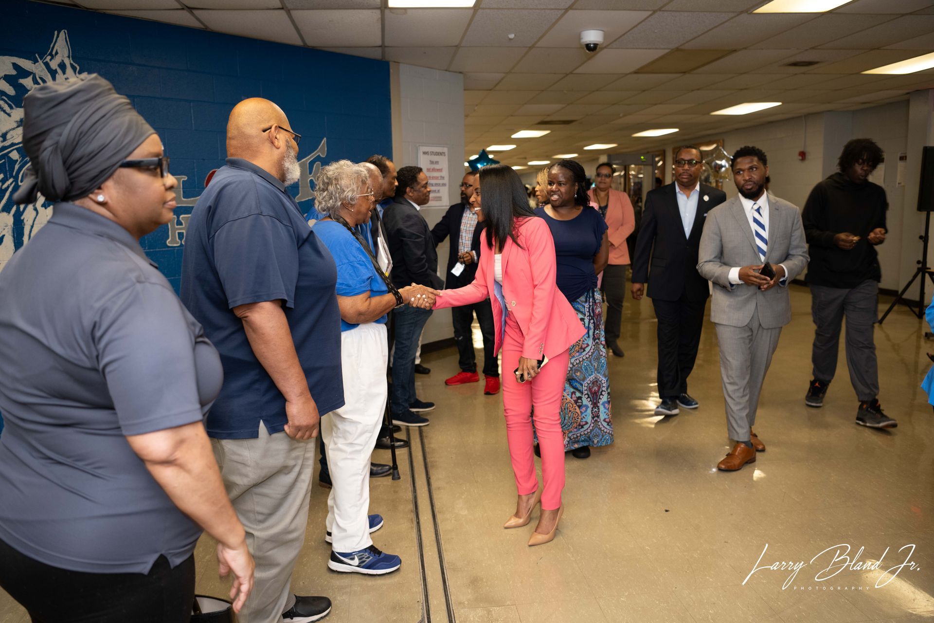 People shaking hands in hallway with blue wall, two people in suits.