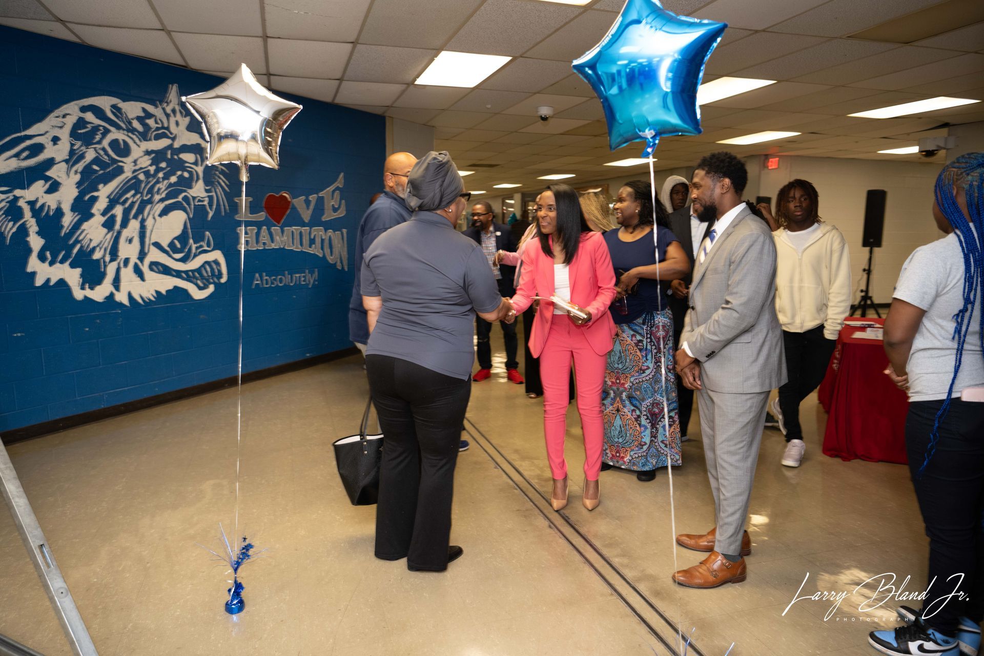 People greeting in front of a school mural with star-shaped balloons.