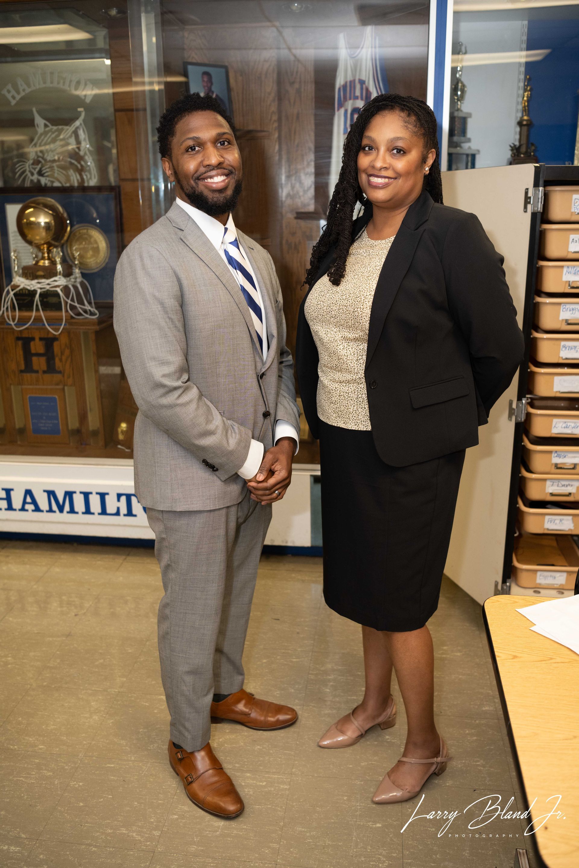 Two people in professional attire stand inside a building.