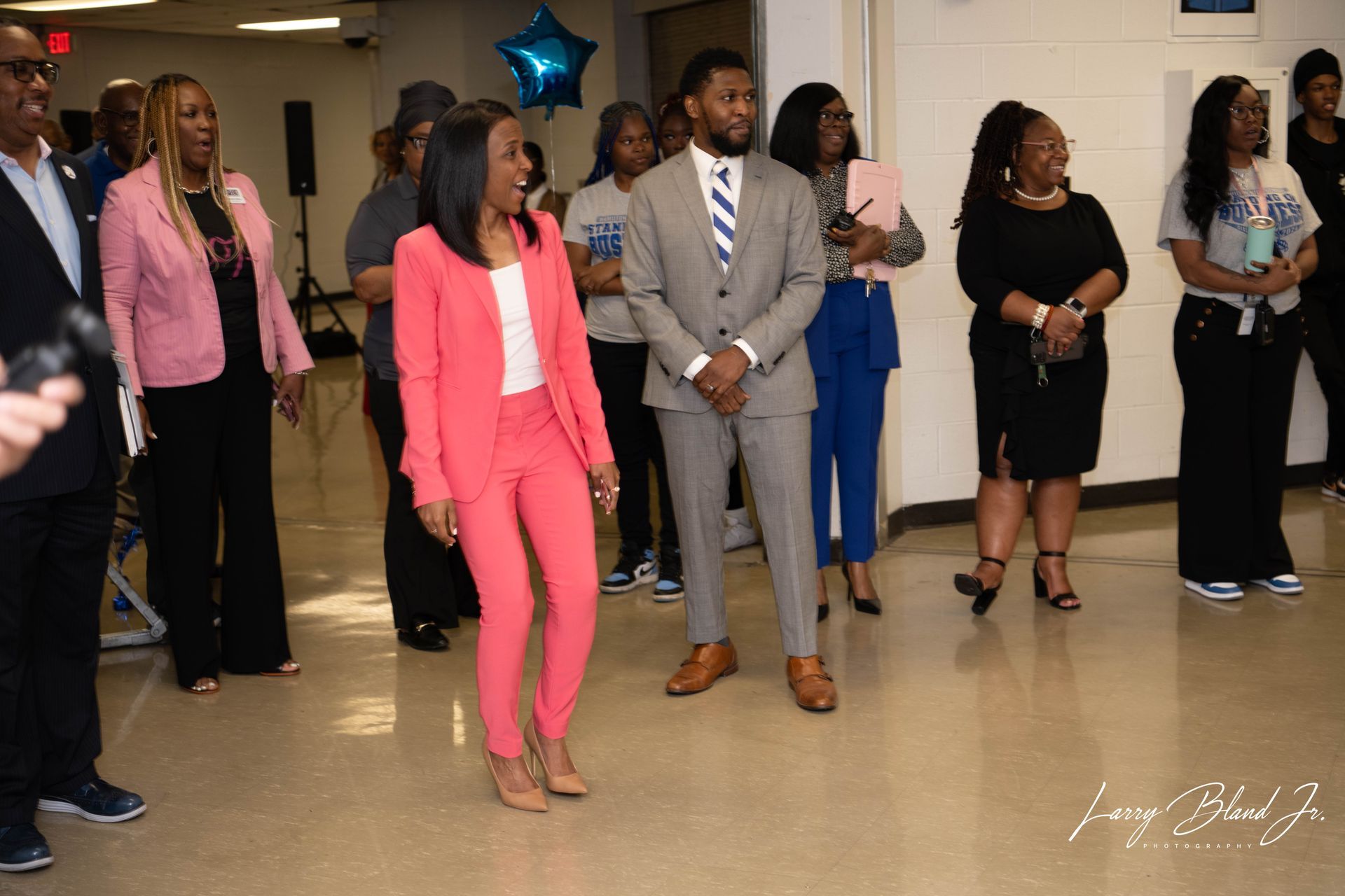 People in a room, some smiling. A person in pink suit, blue star balloon.