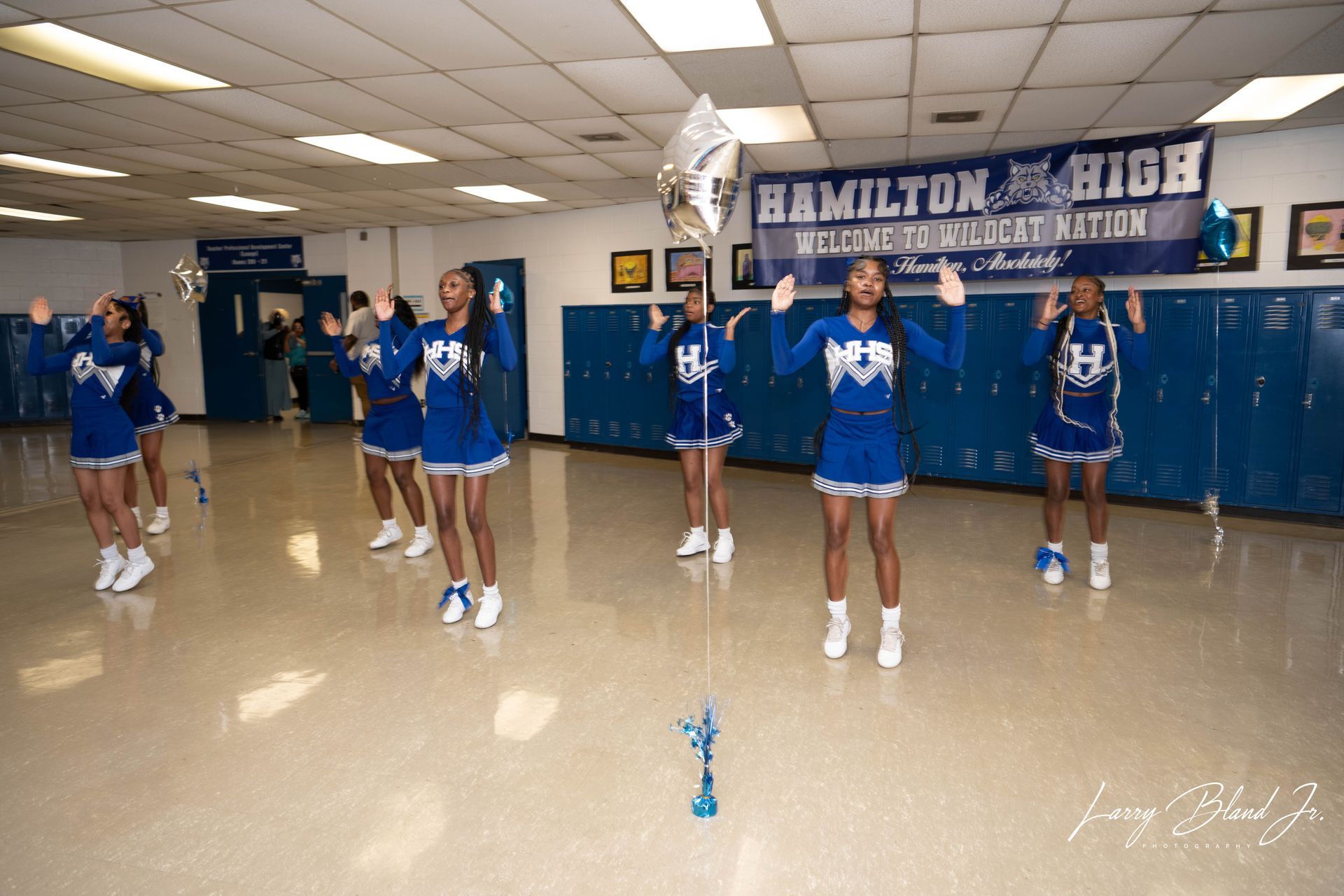 Cheerleaders in blue and white uniforms performing in a hallway with 