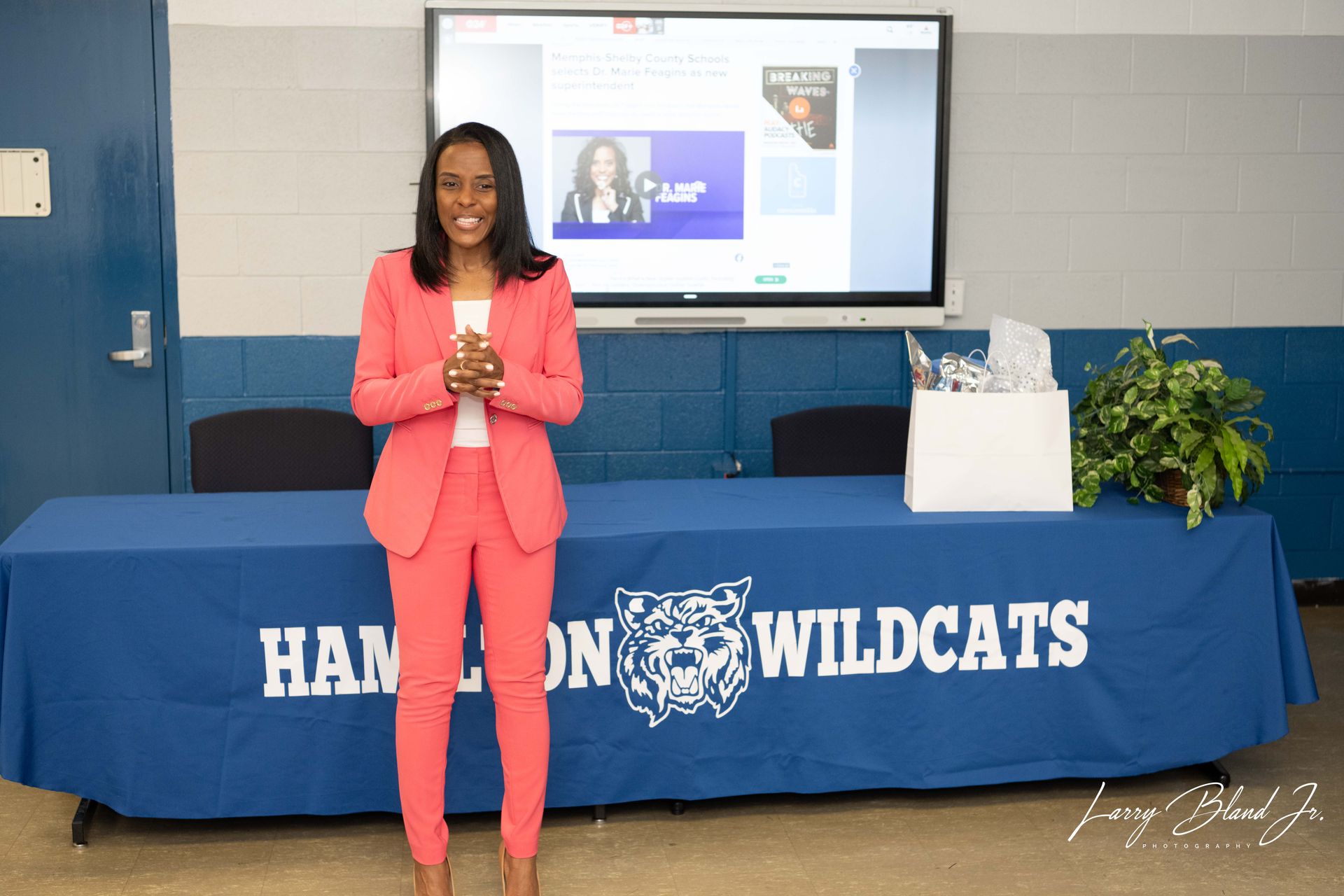 Woman in pink suit, smiles, stands behind table with 