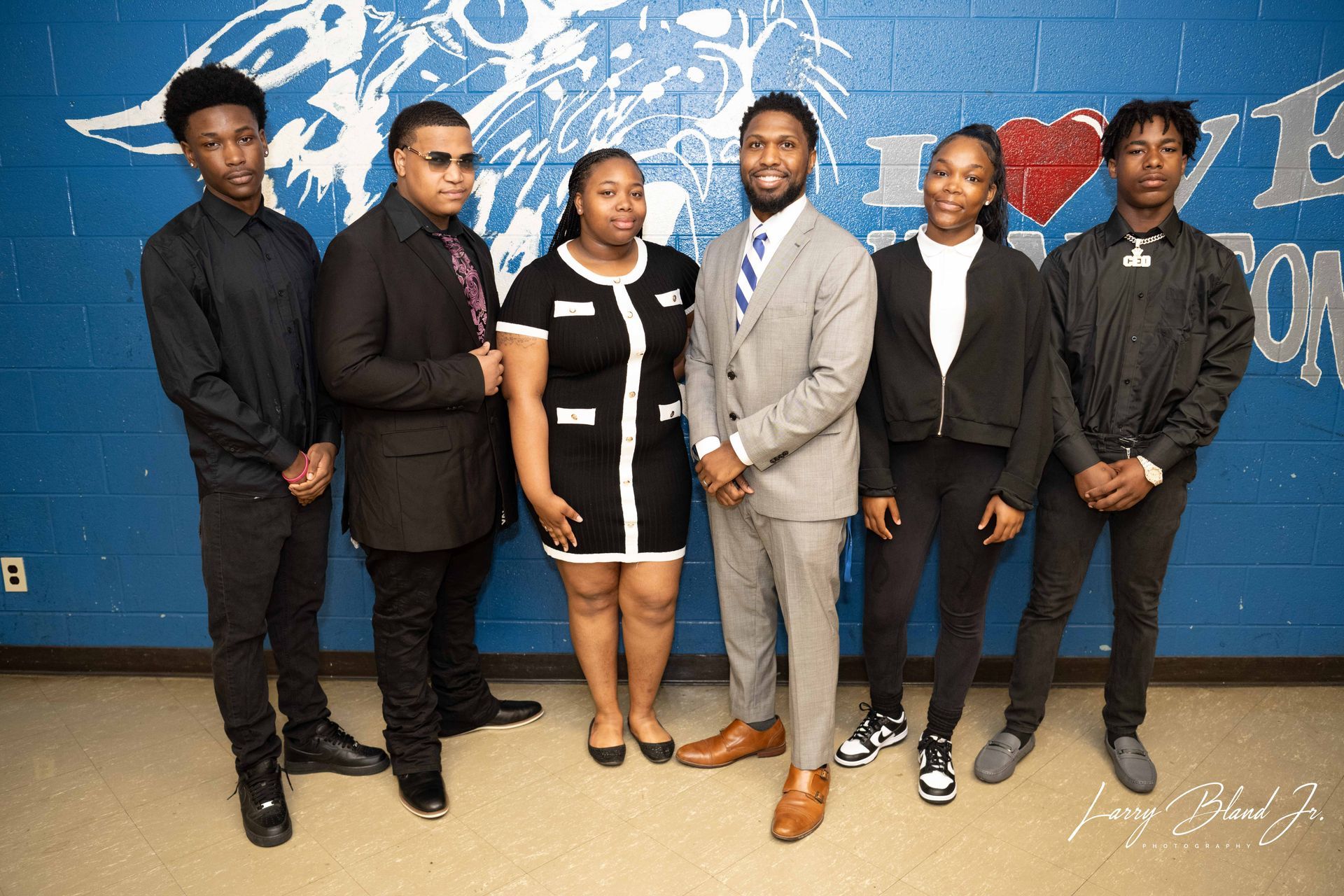 Group of people in business attire posing in front of a blue wall with a school logo.