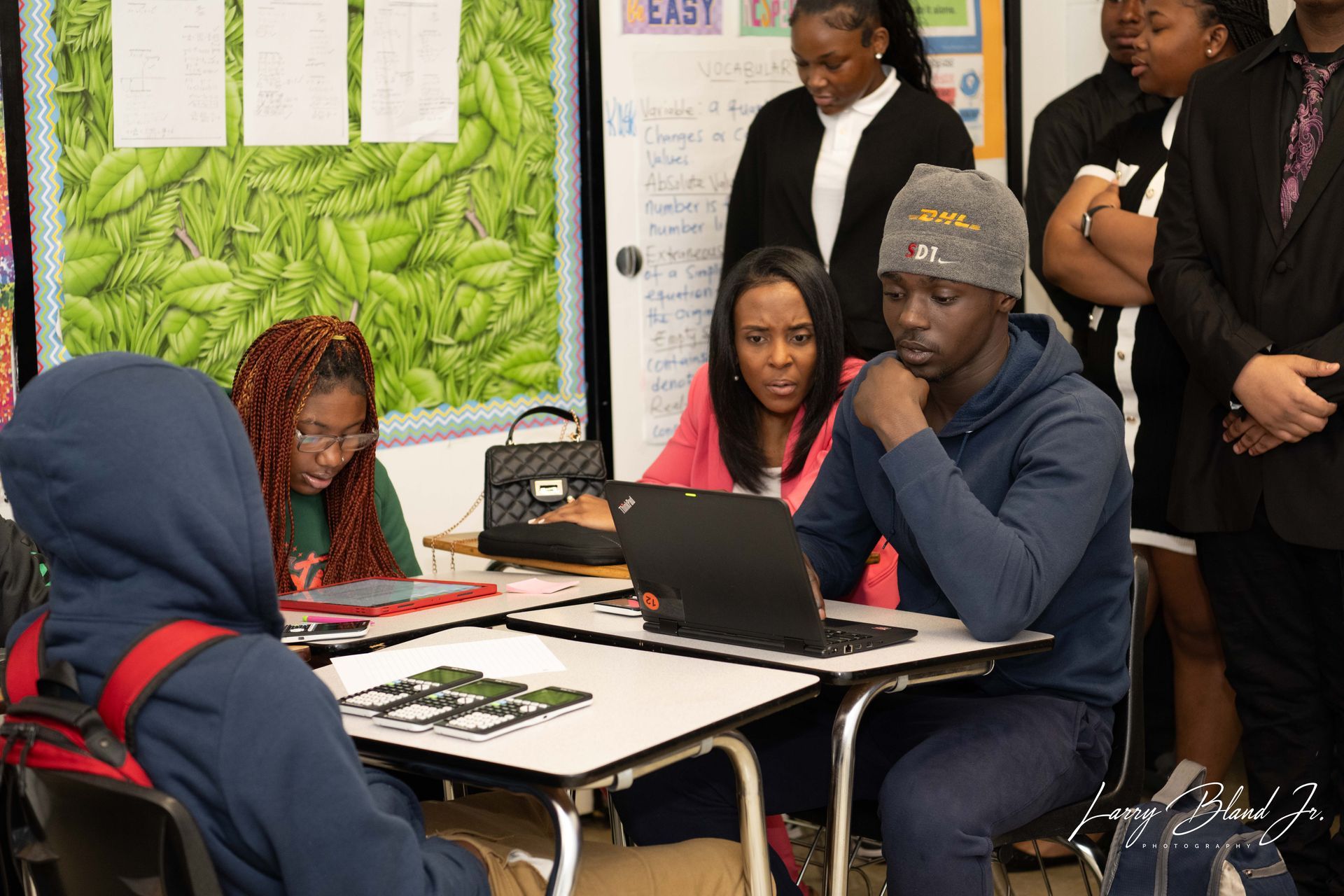 Students and adults in classroom working at desks. One uses a laptop.