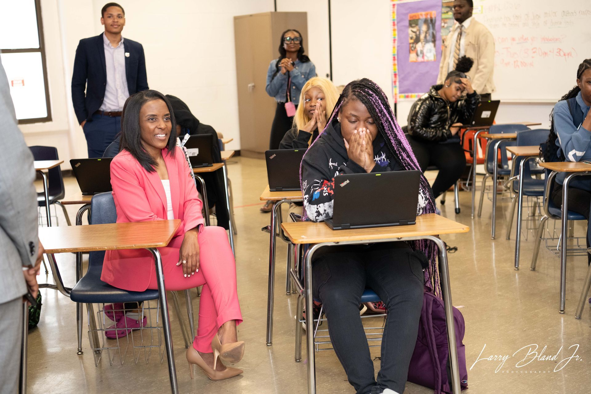 People in classroom; students with laptops, adults observing.