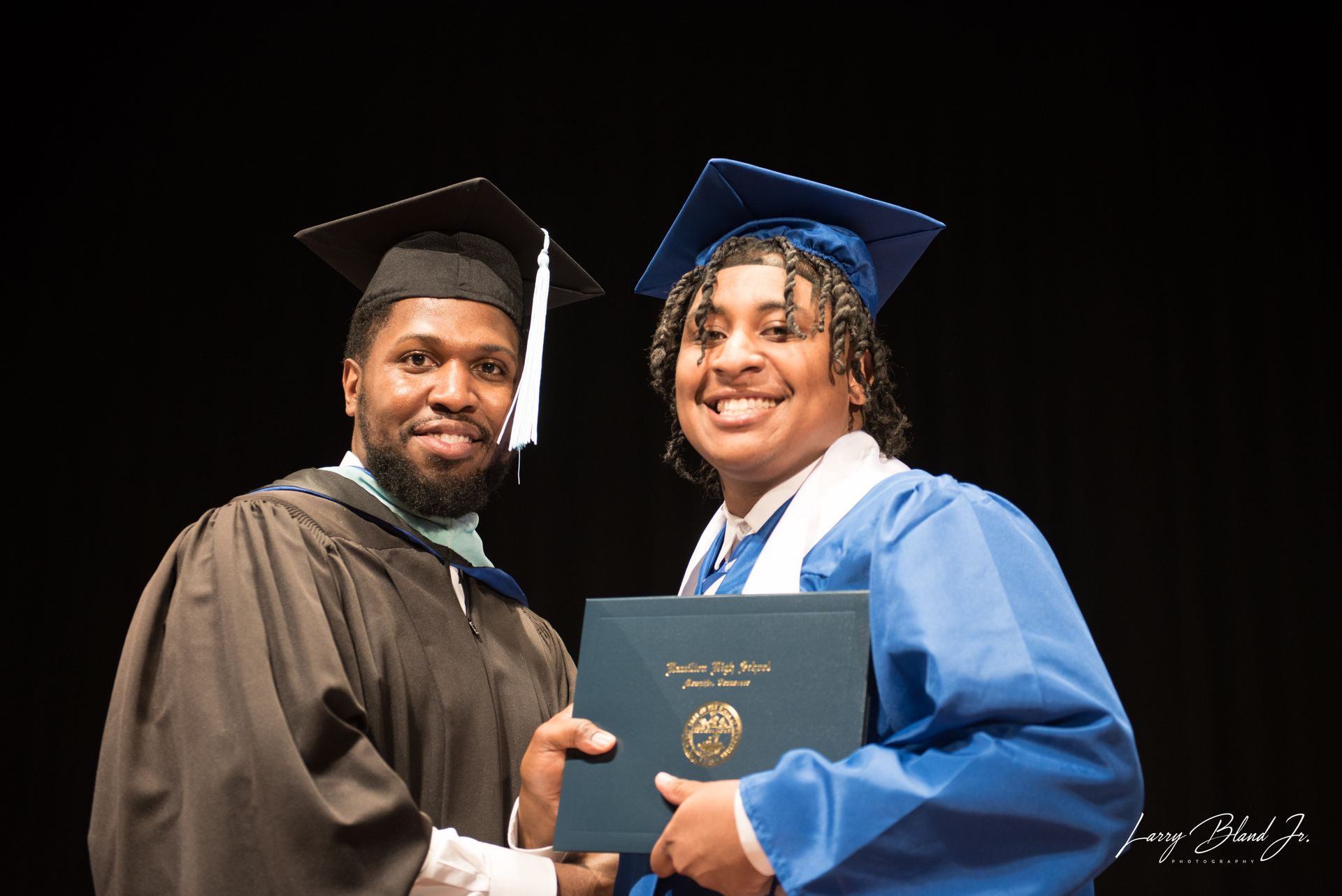 Graduate in blue gown receives diploma from robed person.