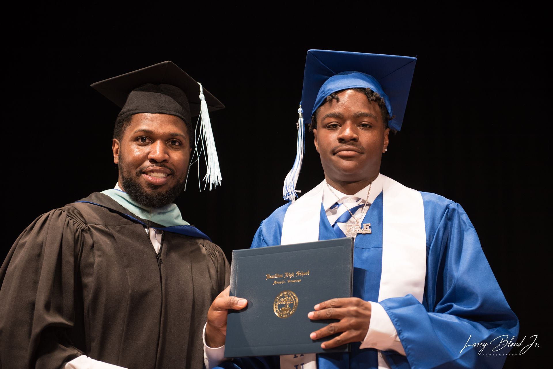 Two people in graduation attire, one handing a diploma.