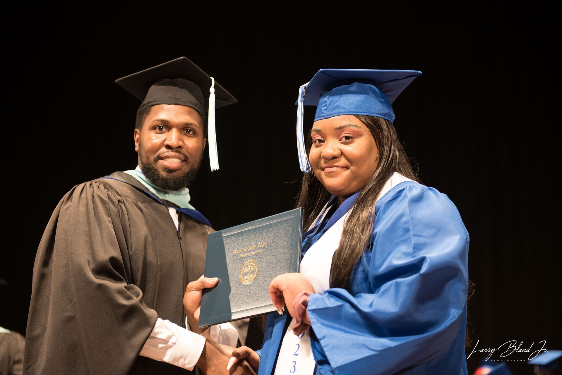 Graduation ceremony: A person in a blue gown receives a diploma from a person in academic regalia.
