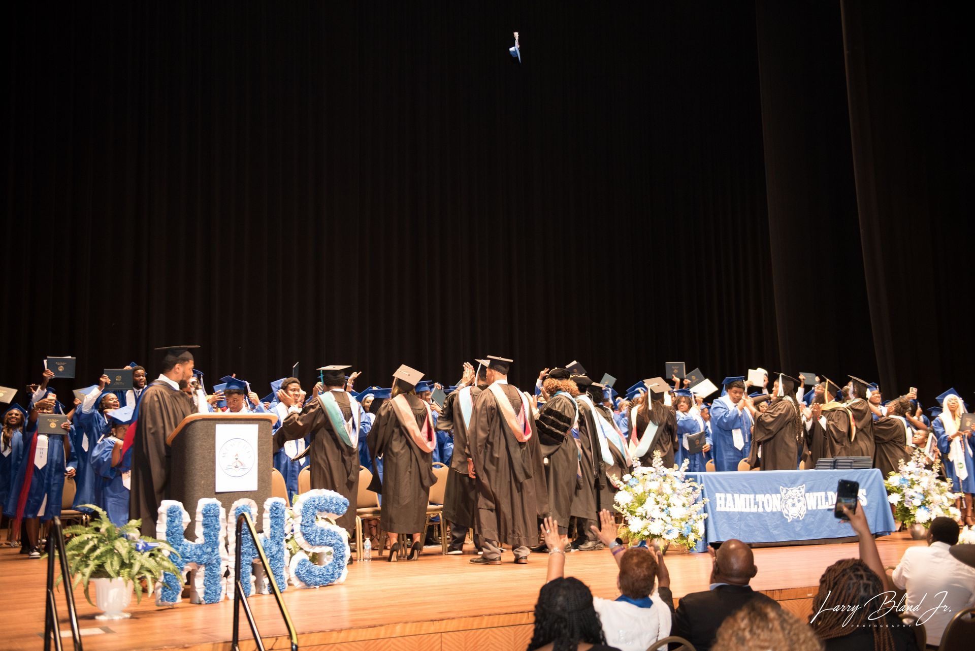 Graduation ceremony with graduates tossing caps. Stage with 