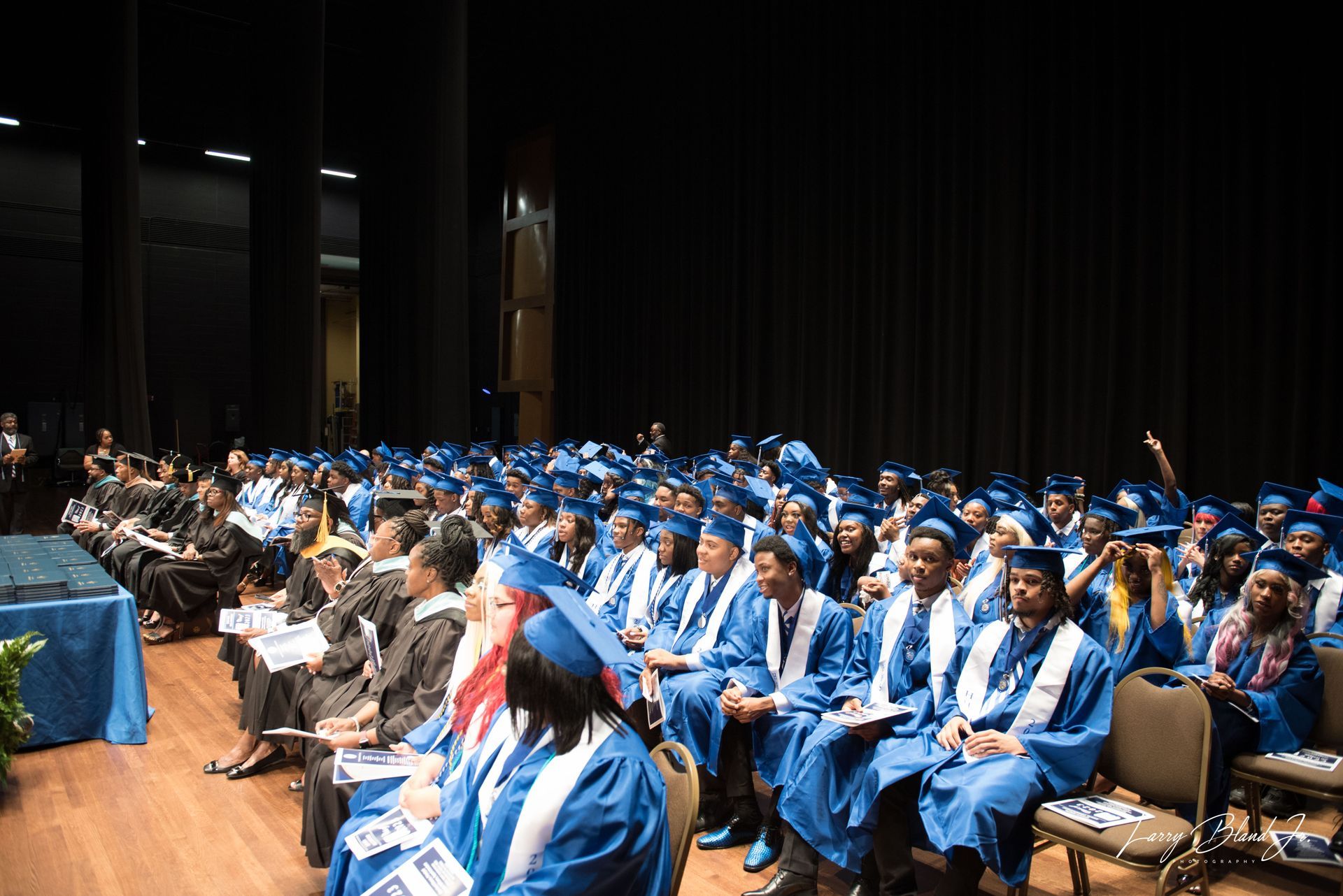 Graduation ceremony with students in blue gowns seated in an auditorium.