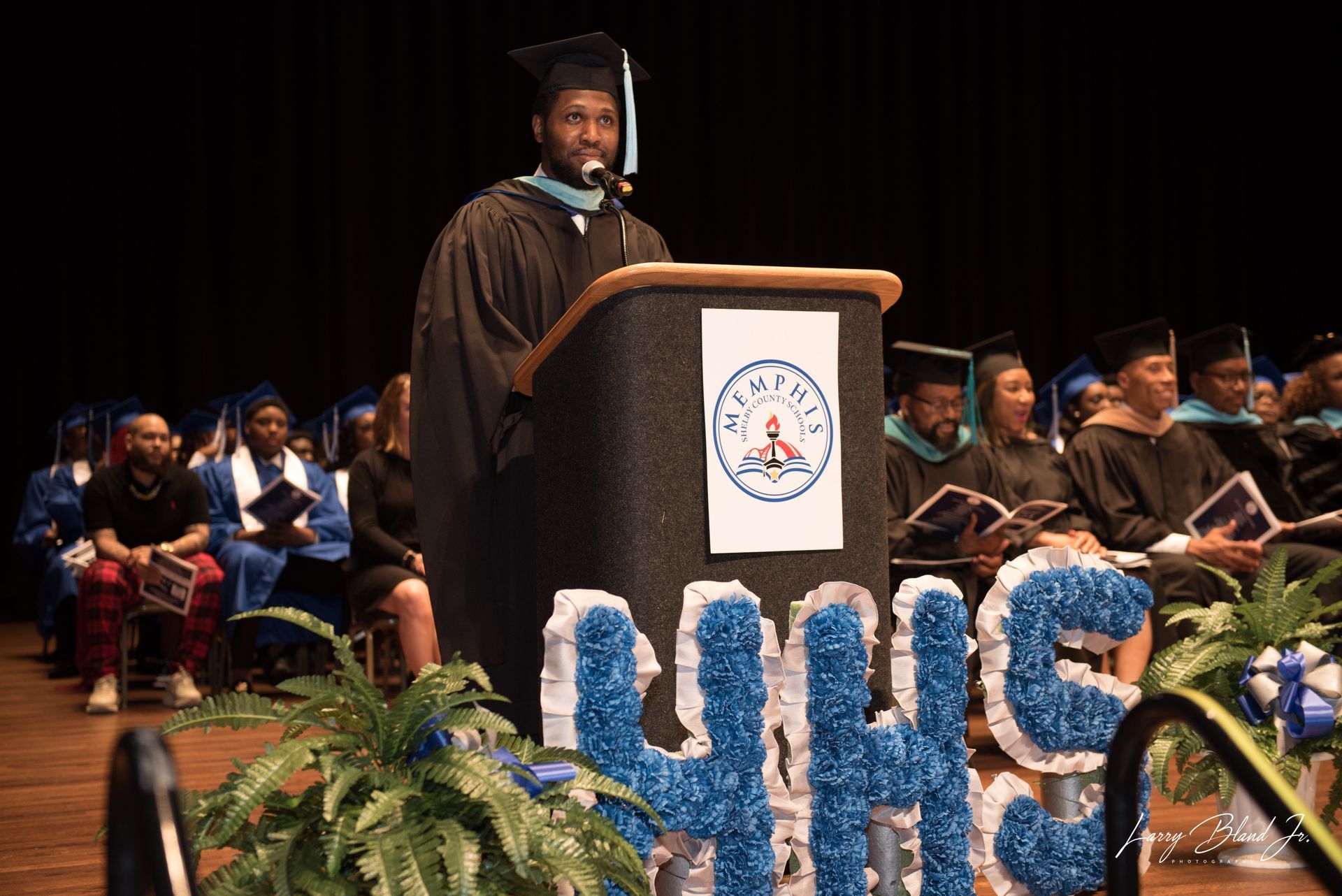 Person in graduation gown speaking at a podium, 