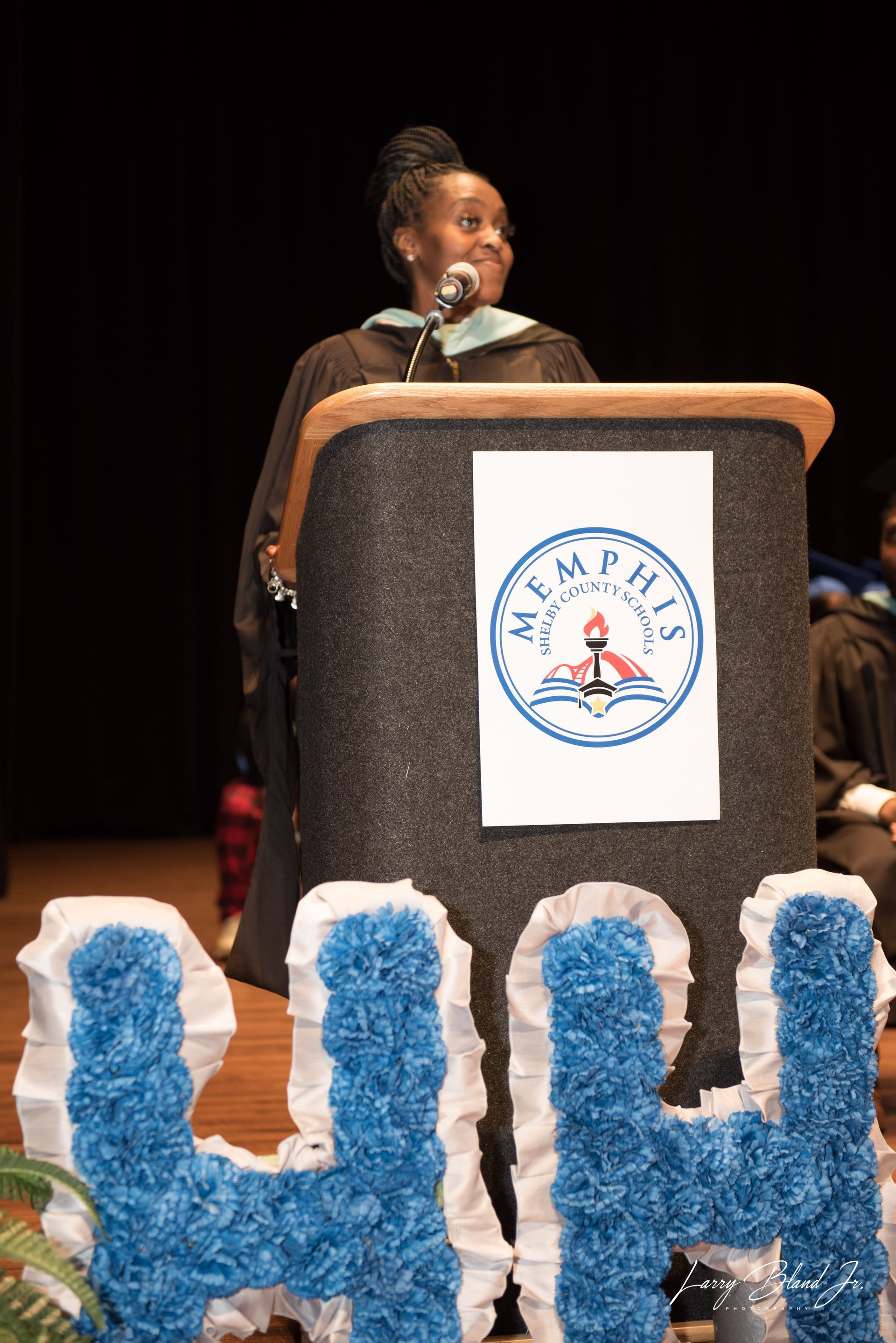 Person in graduation attire speaks at a podium with 