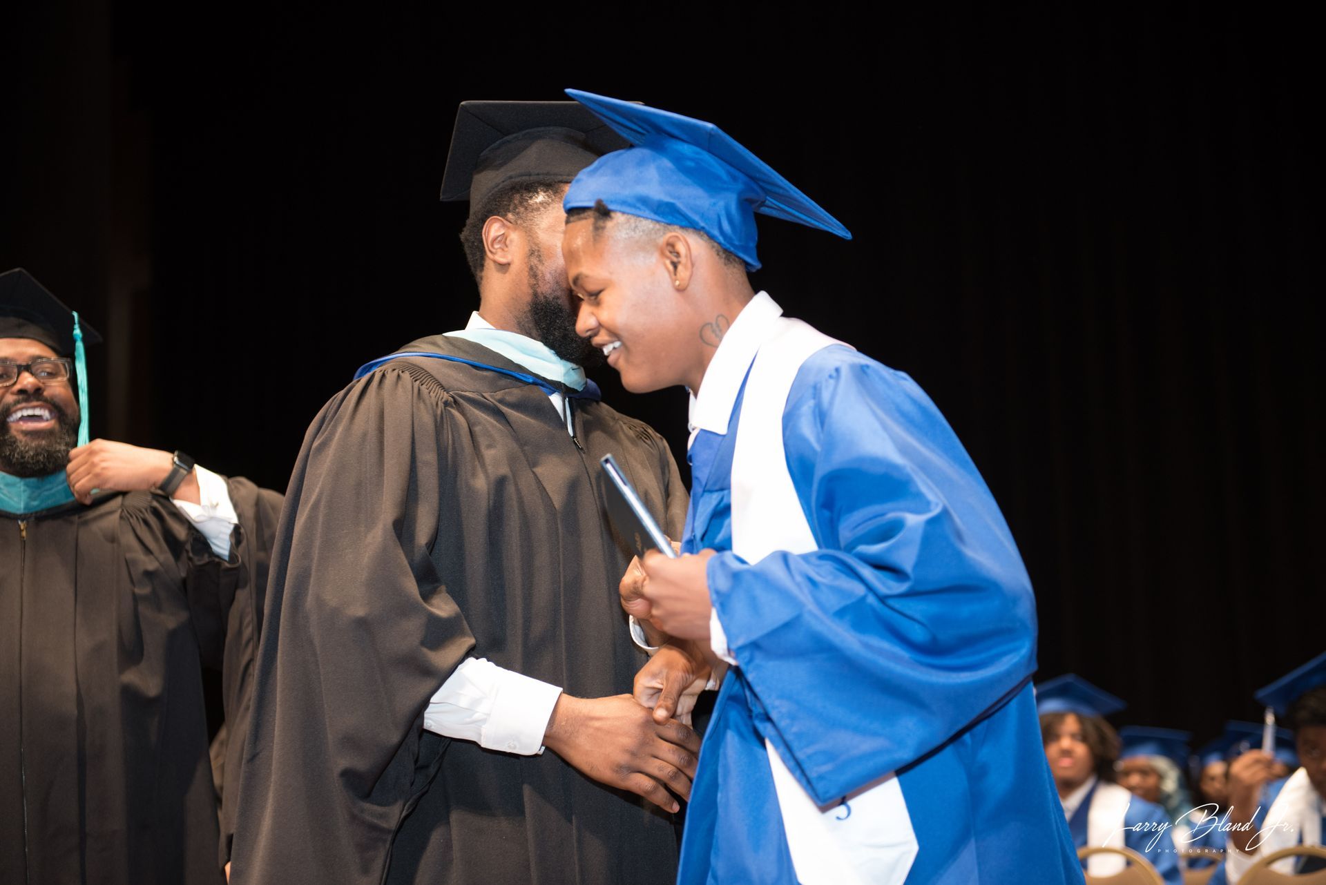 Graduation ceremony: Man in cap and gown shakes hands with graduate in blue gown.