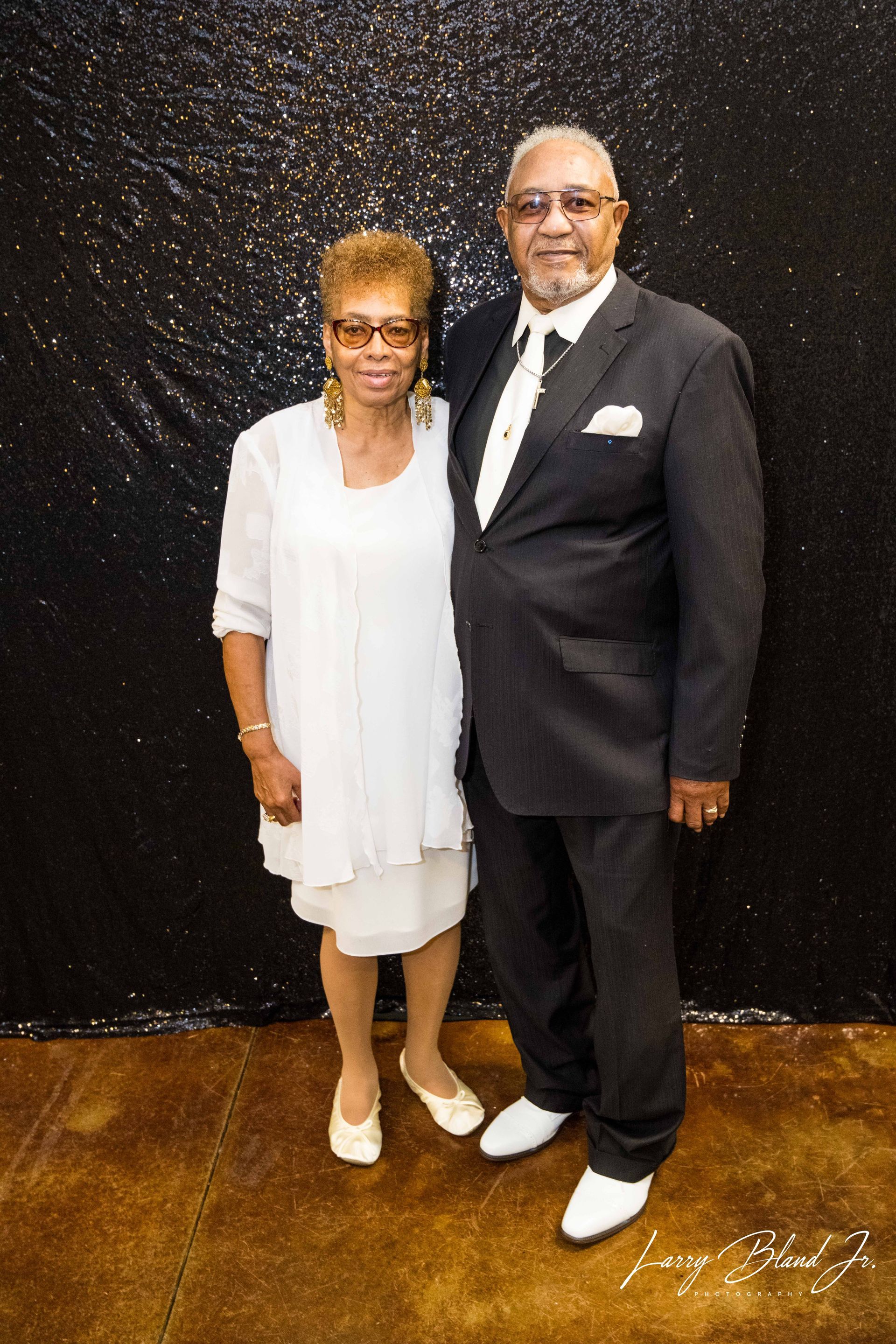 Couple in formal attire posing in front of a sparkling black backdrop.