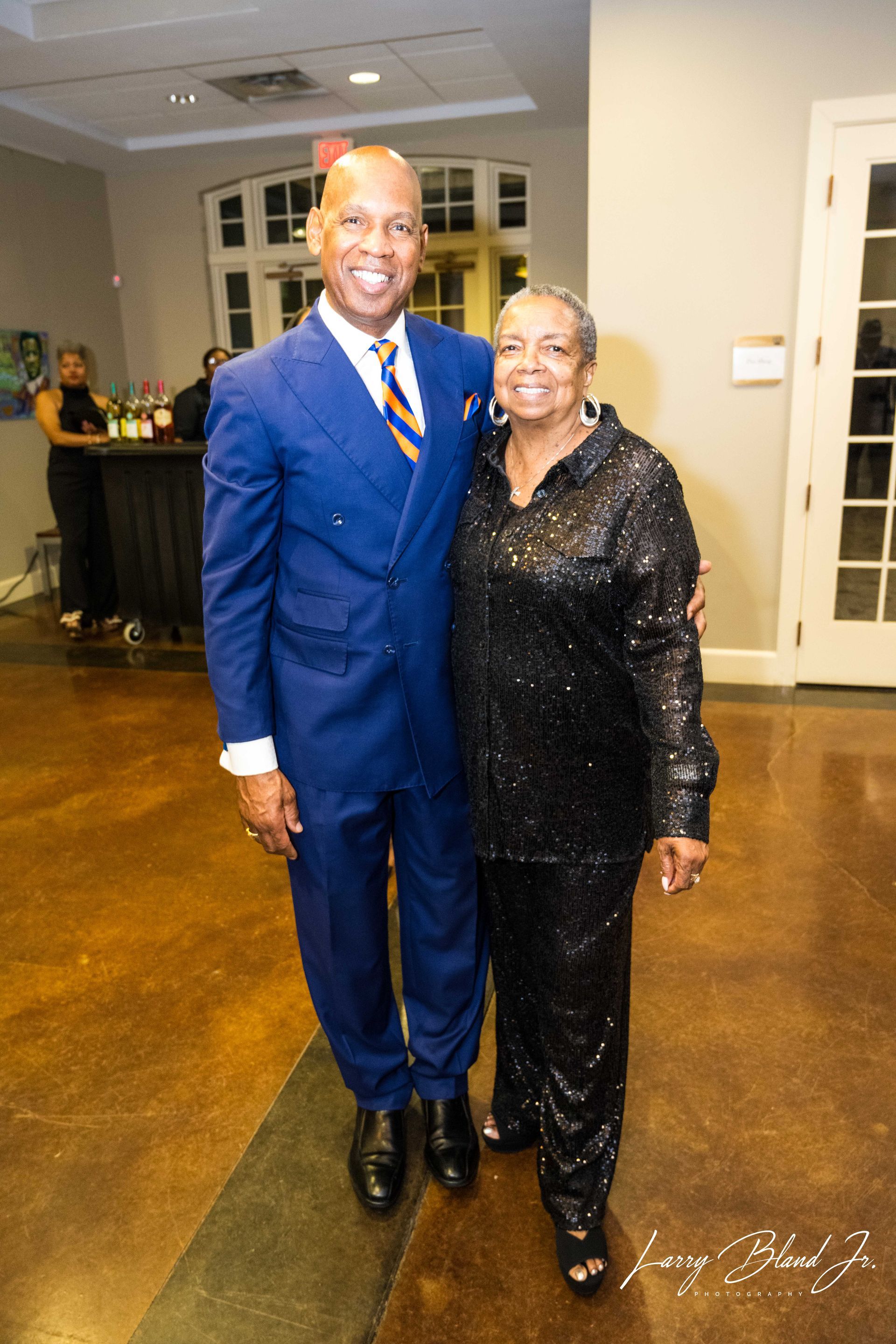 Man in blue suit and woman in black sequin outfit posing together at an event.