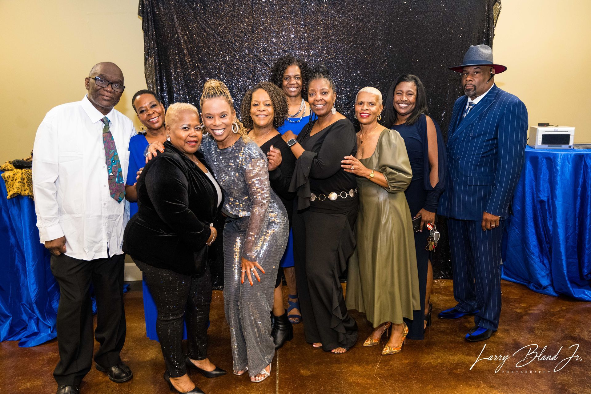 Group of people posing at an event. Some are smiling, wearing formal attire, standing in front of a blue and black backdrop.
