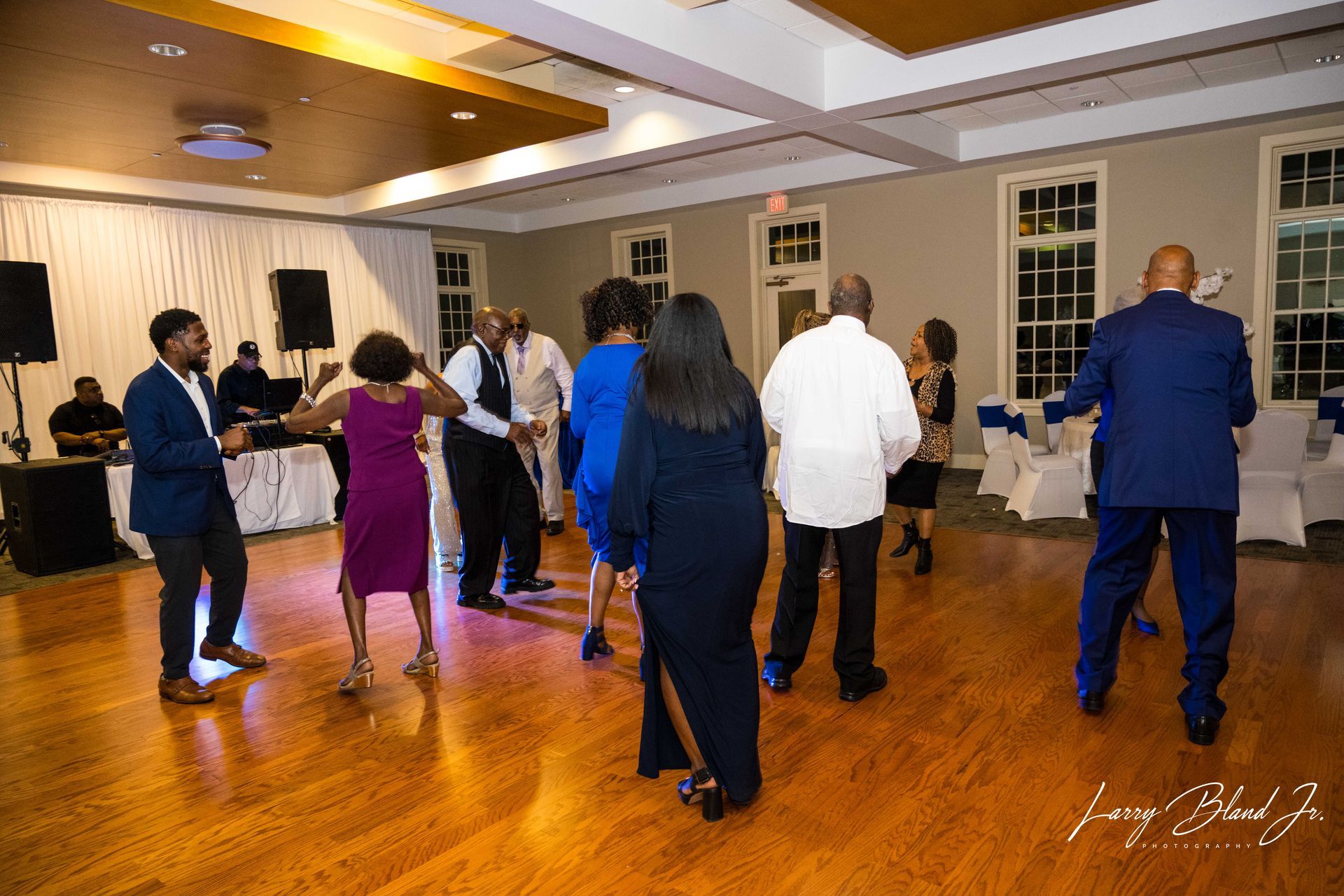 People dancing at an event in a well-lit room with wooden floors.