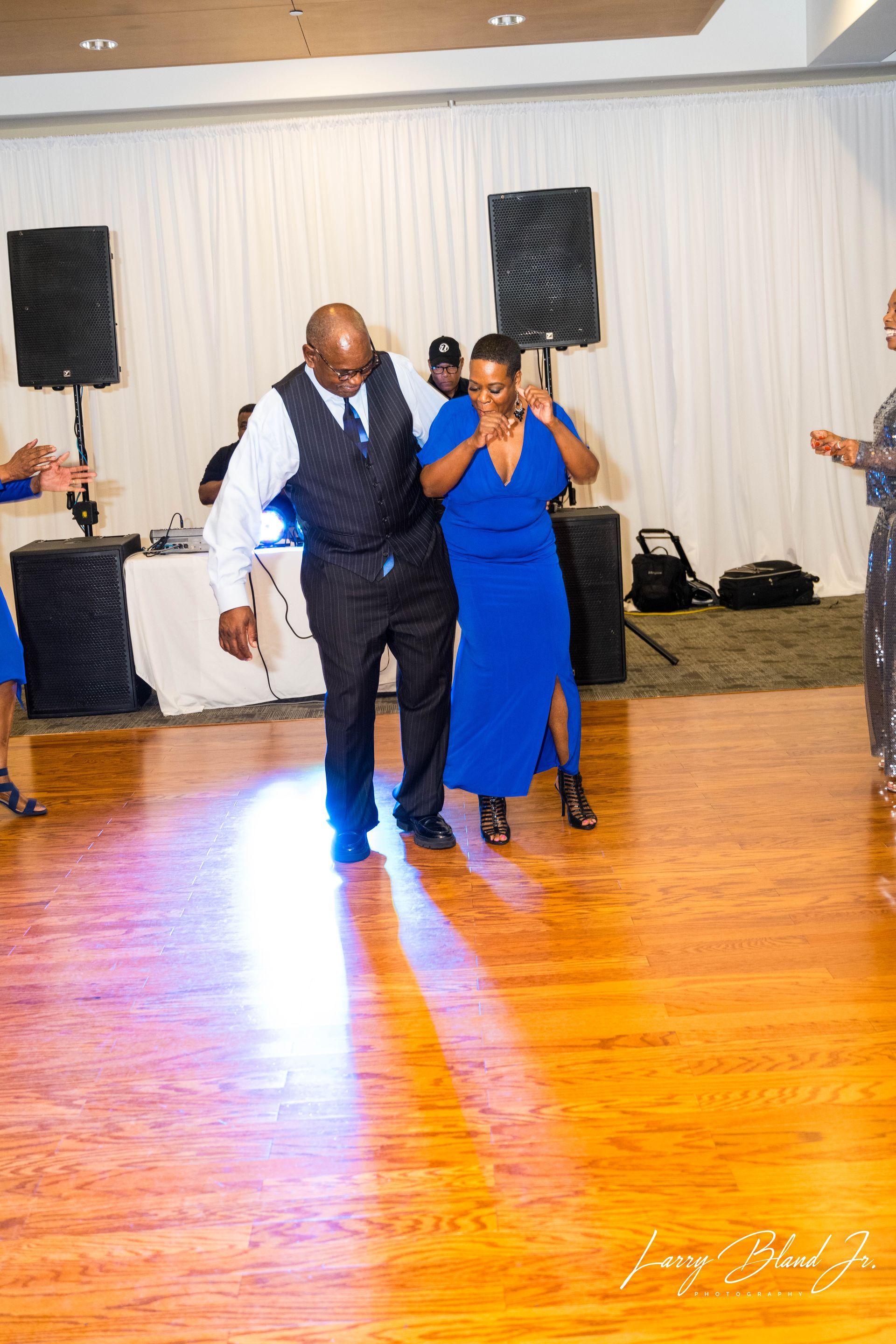 Couple dancing on a wooden floor at an event, with music equipment in the background.