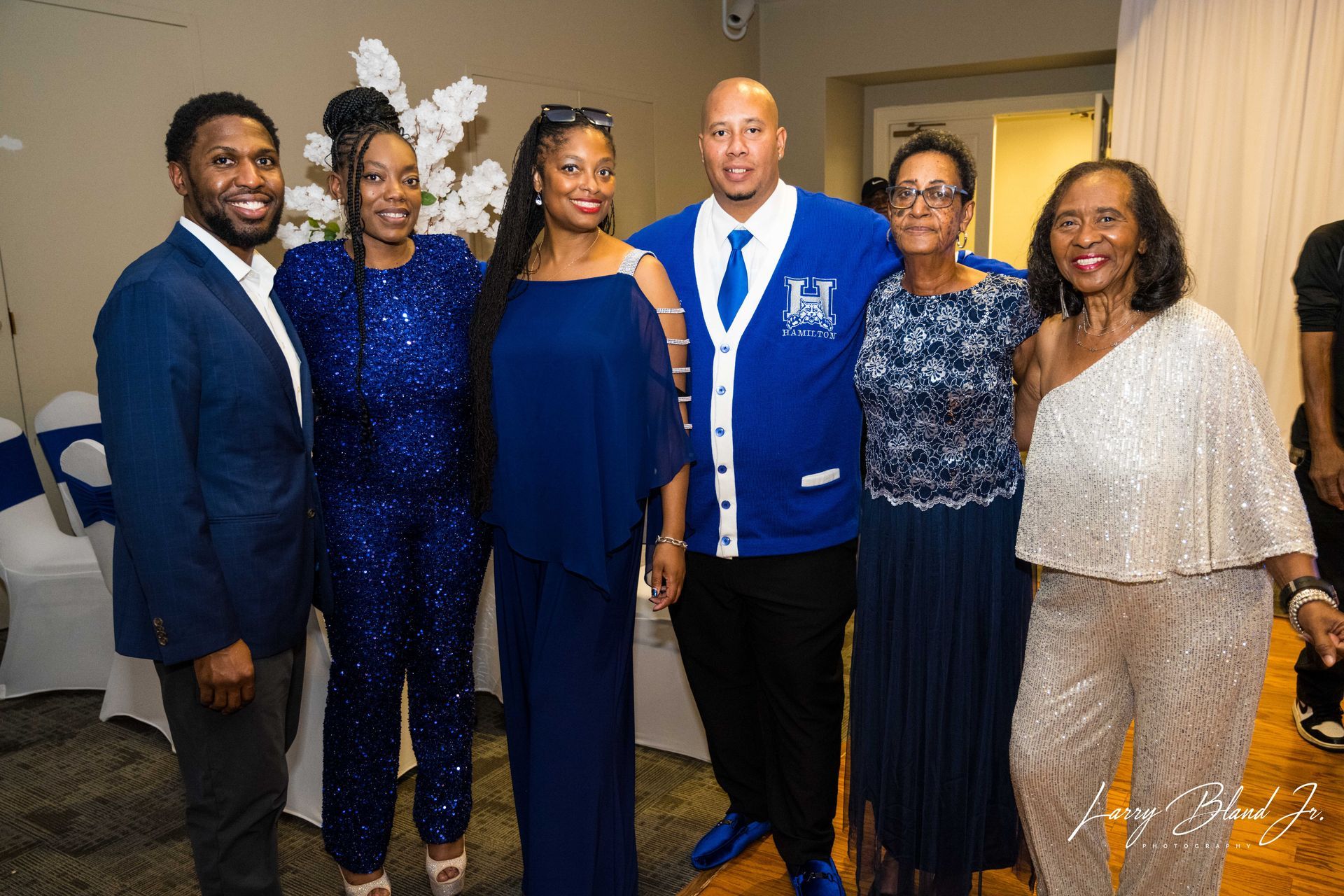 Group of people in formal attire pose together at an indoor event. Predominantly blue colors.
