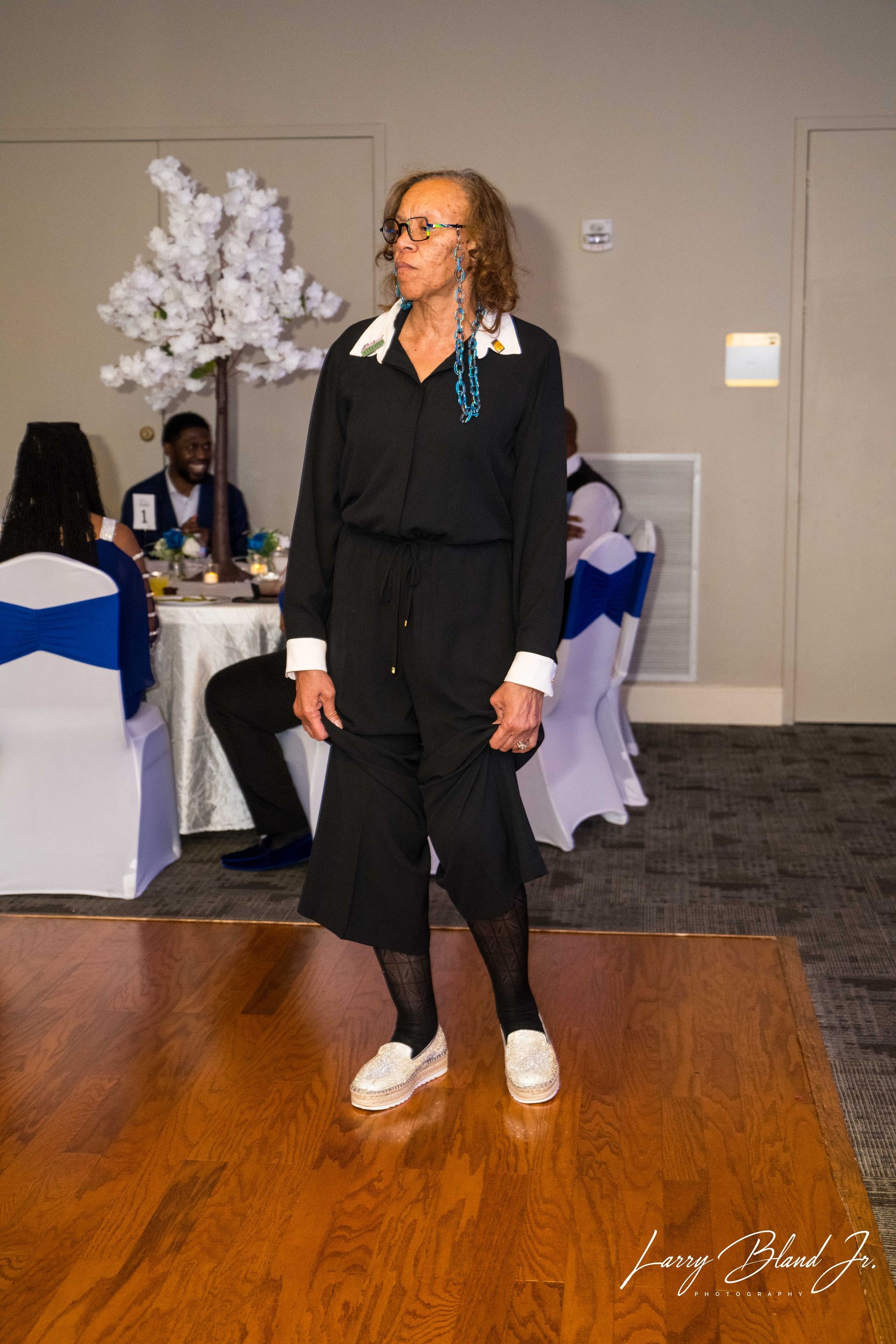 Person in black outfit on a dance floor, white sneakers. Event with tables and decorations.