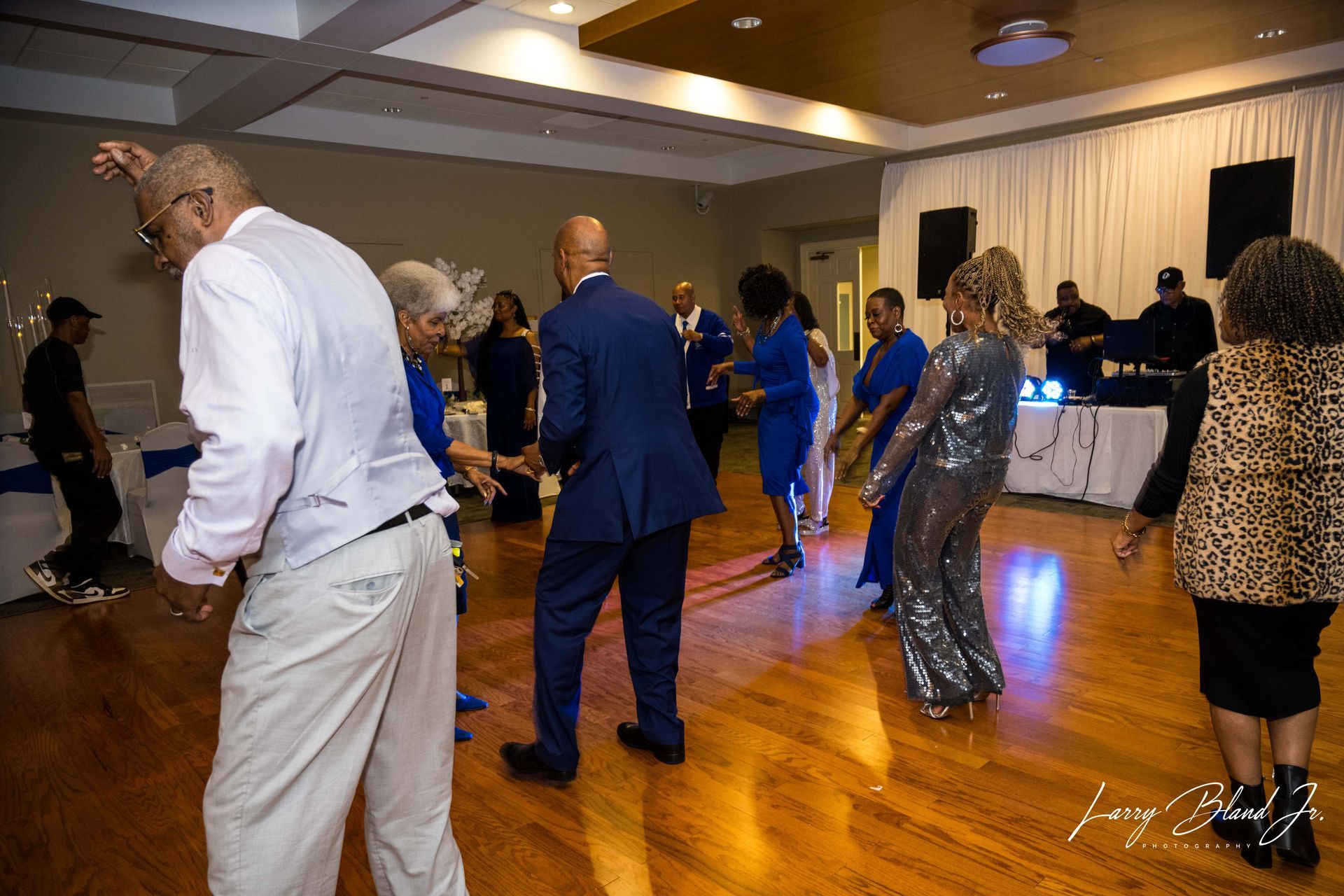 People dancing in a brightly lit ballroom. Some are wearing blue and silver outfits.