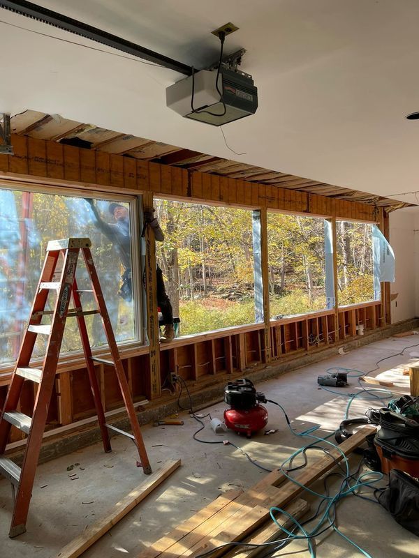 Garage interior renovation: Windows framed, ladder, air compressor, debris on the floor, garage door opener visible.