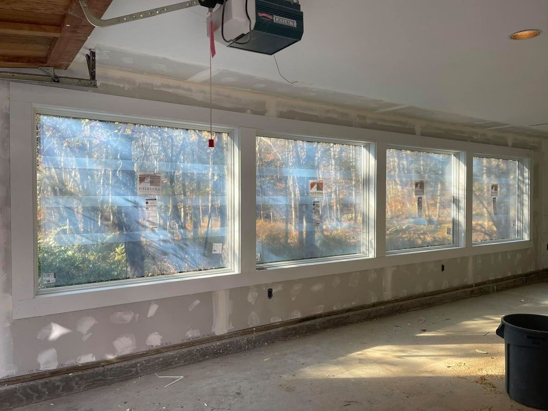 Three large rectangular windows in a room under construction, with visible forest outside.