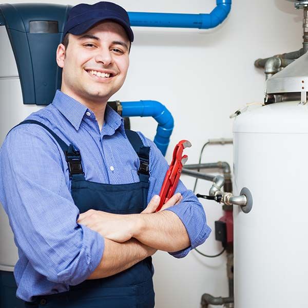 Plumber in blue uniform holding red pliers beside a water heater and pipes.