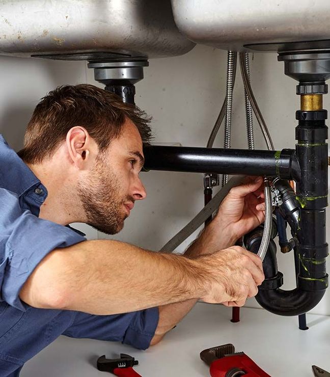 Plumber repairing pipes under a sink with a wrench and tools.