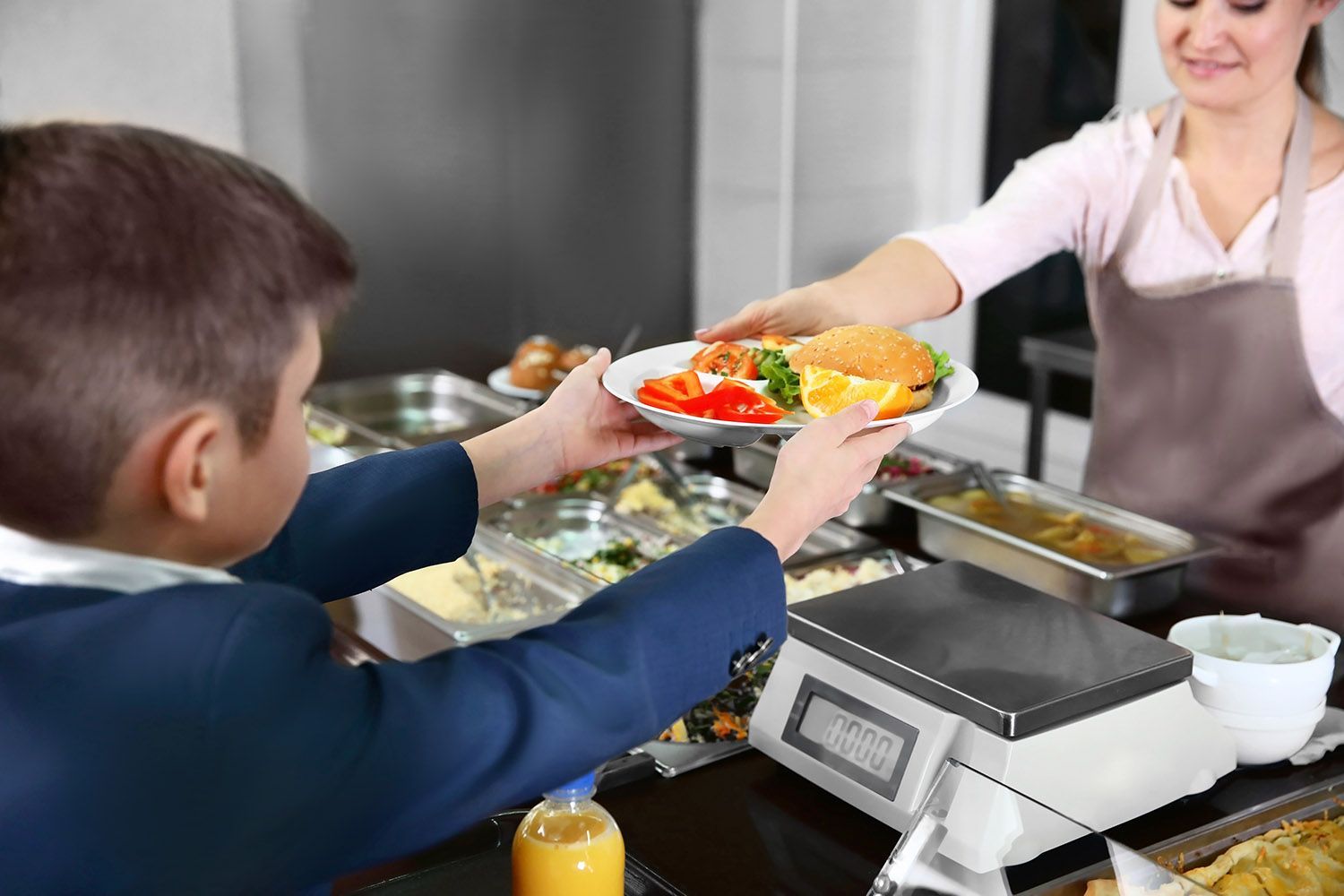 Customer receiving a salad bowl from a cafeteria server at a counter.