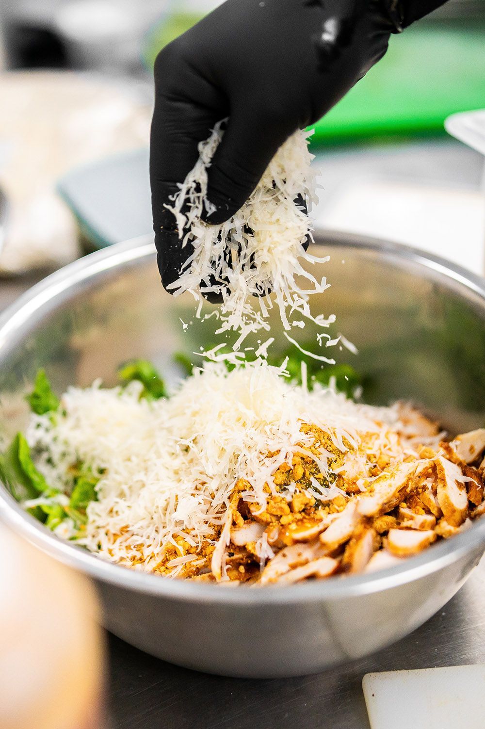 Gloved hand sprinkling shredded cheese over a bowl of rice, chicken, and broccoli