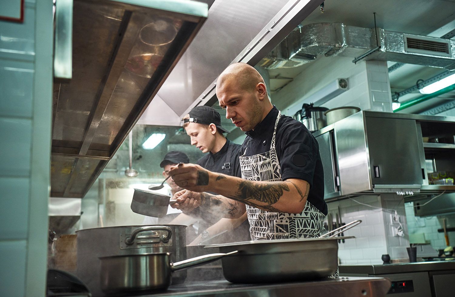 Two chefs plating food in a stainless steel commercial kitchen, focused on preparing dishes