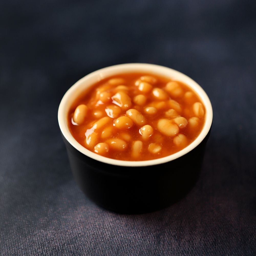 Black cup filled with baked beans on a dark blue cloth background