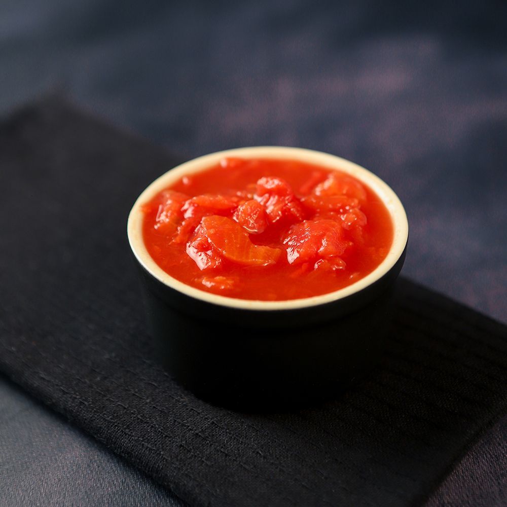 Small white bowl of bright red salsa on a dark napkin
